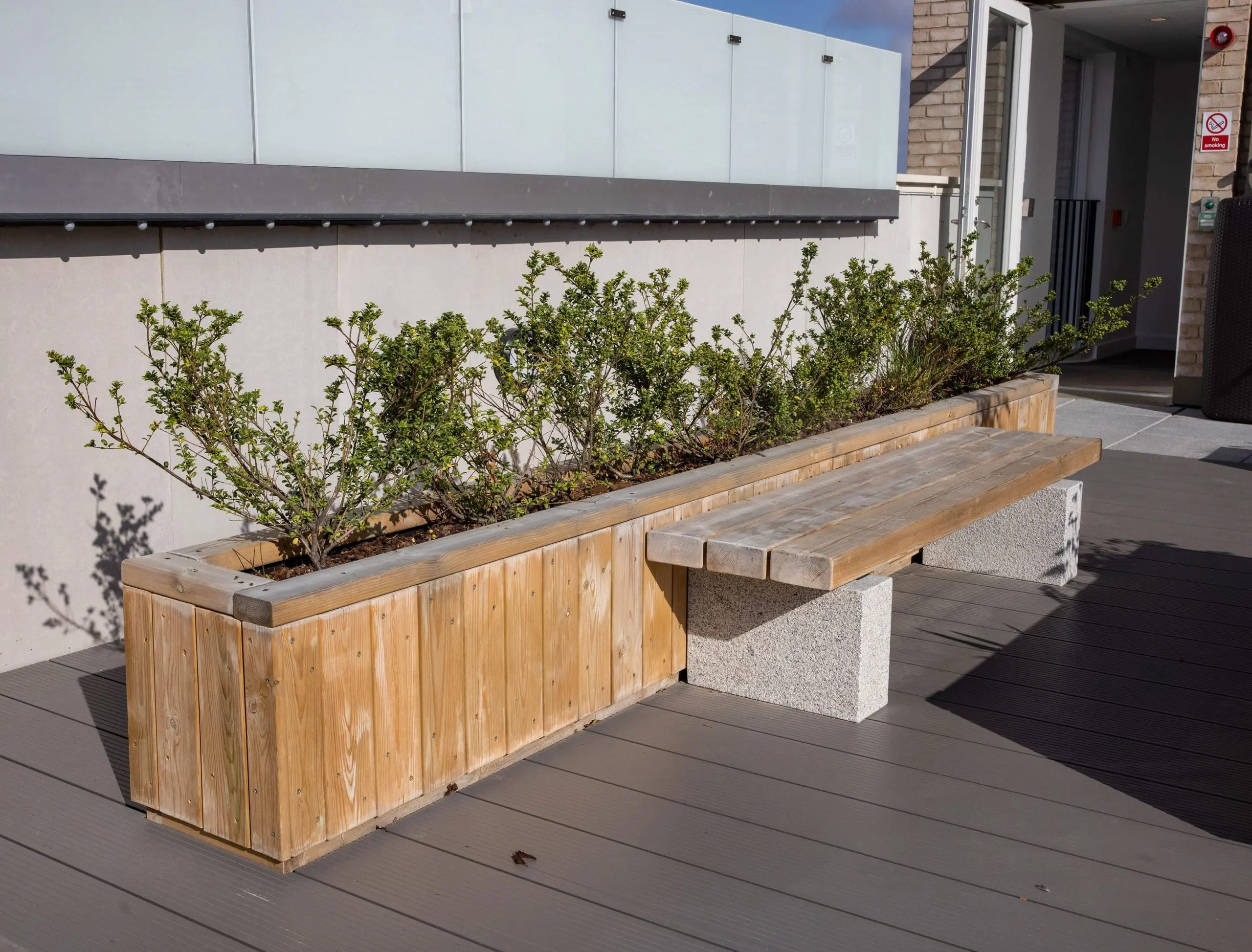 outdoor rooftop wooden planter behind wooden bench with concrete plinth legs