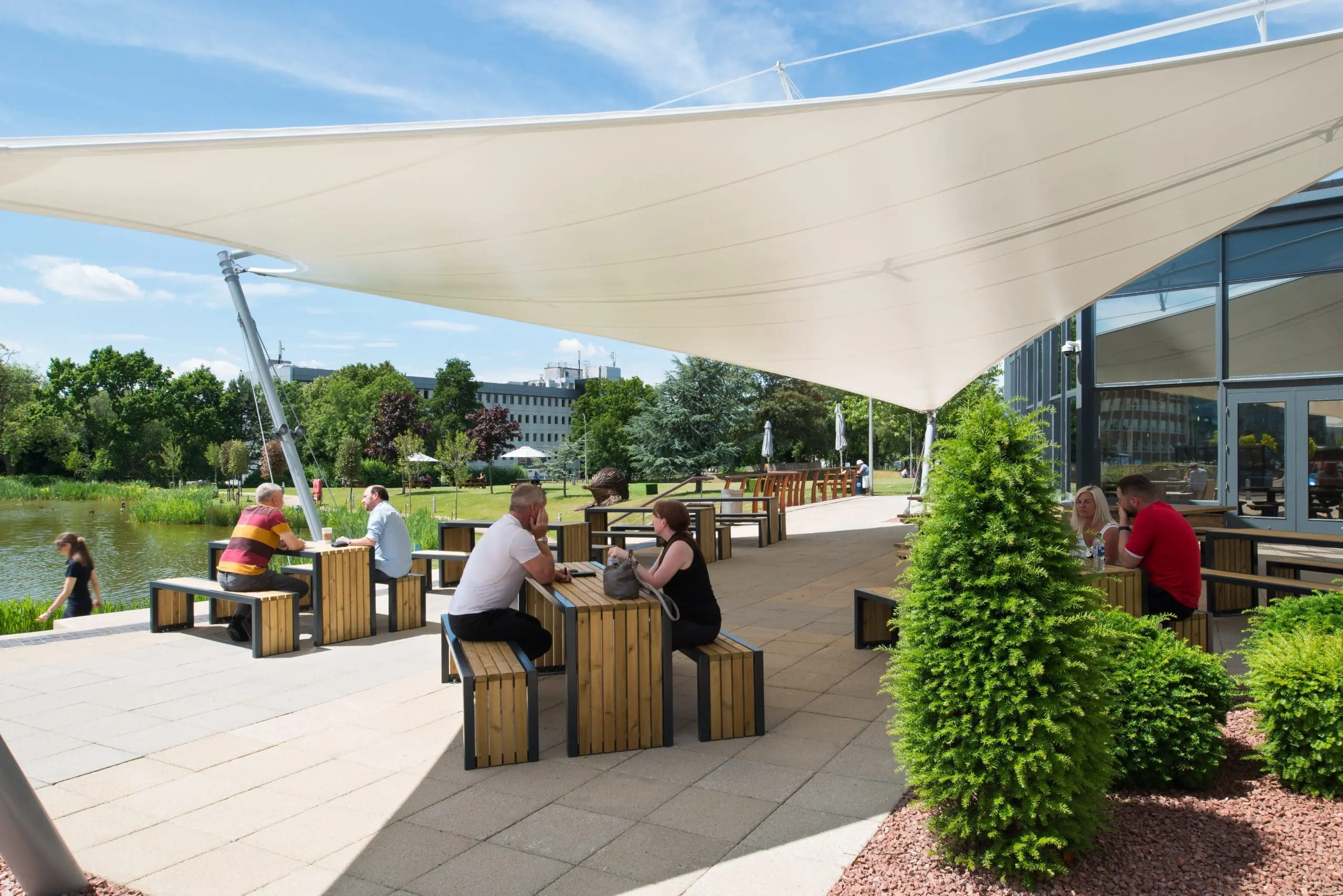 wooden-steel-framed-picnic-tables-and-chairs-under-large-stretch-canopy-with-people-sat-around