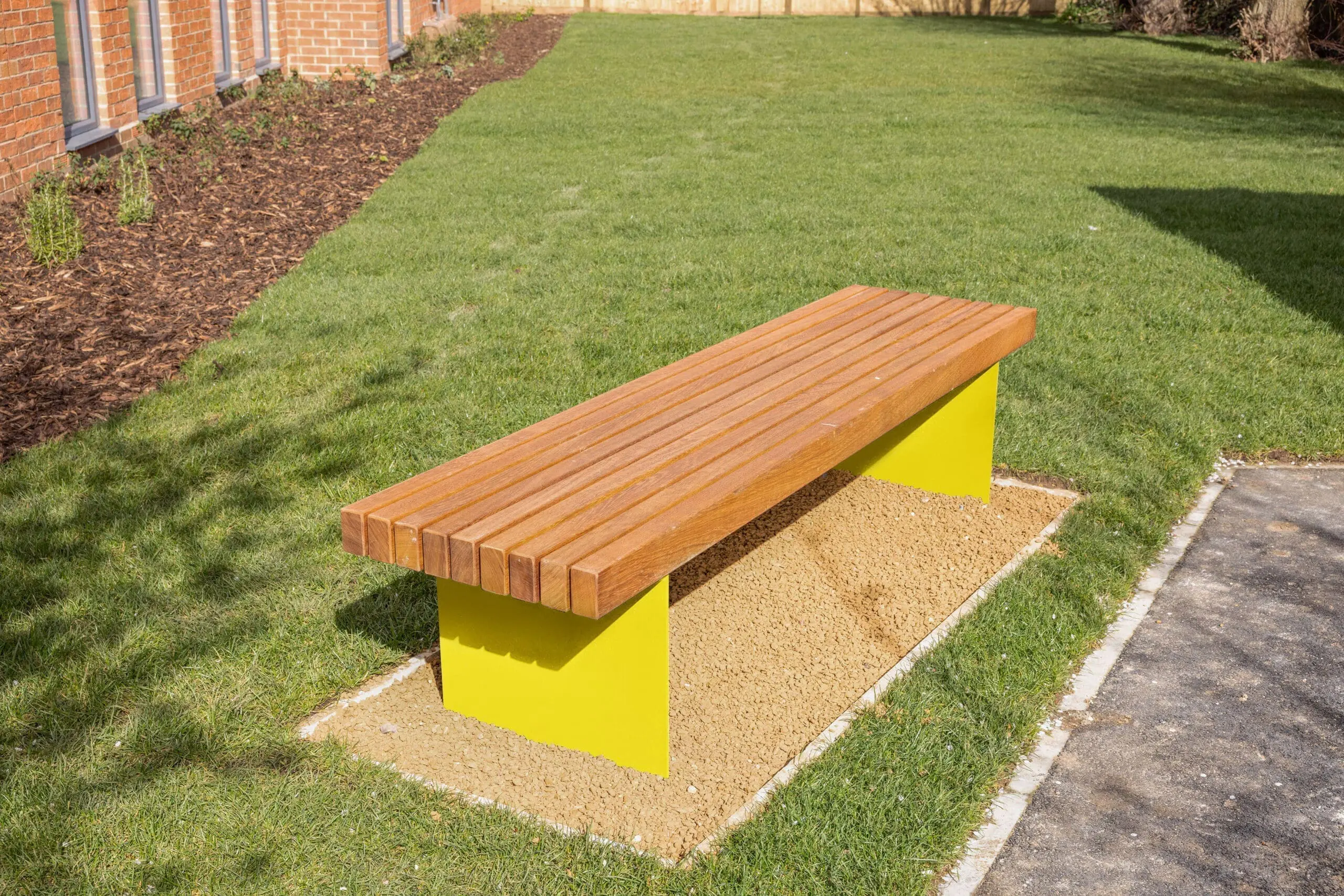 Wooden bench with yellow wooden legs, sat on a patch of grass on a sunny day.