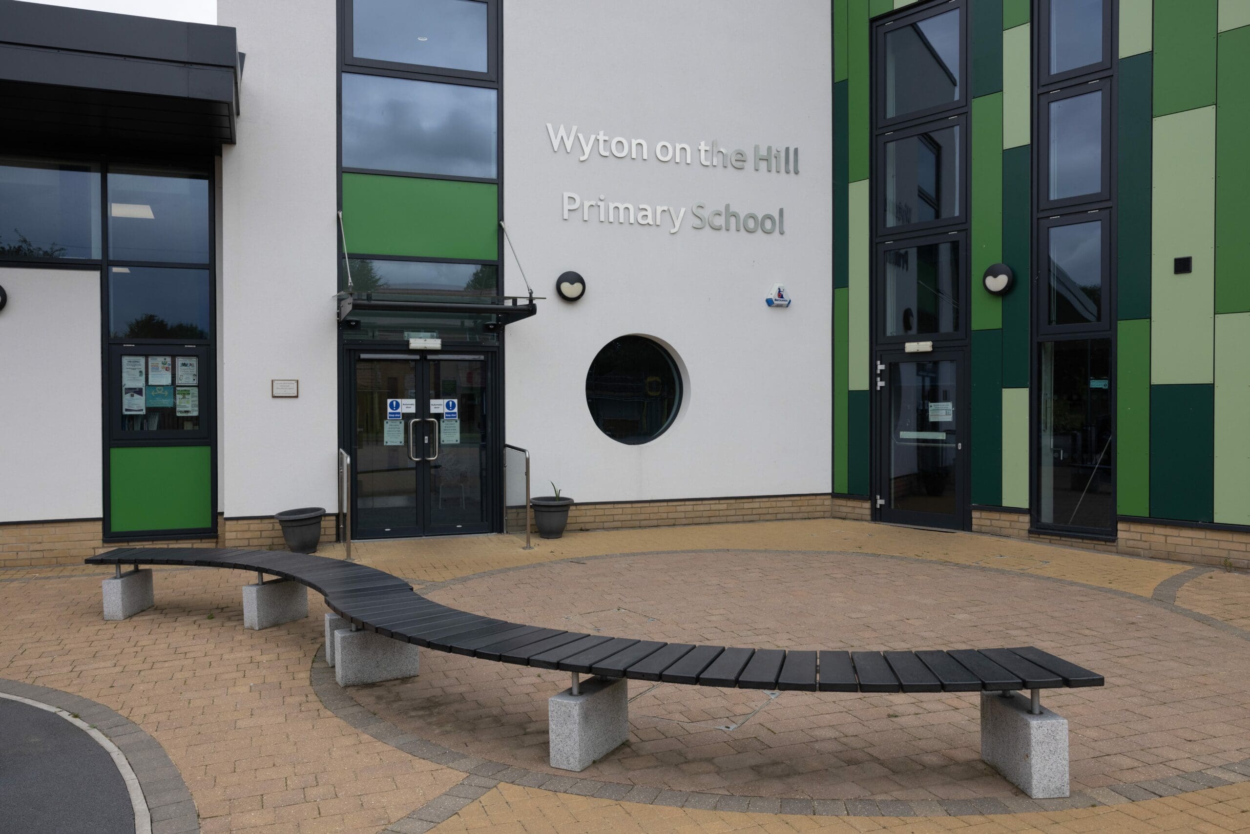 S shaped curved outdoor bench black wood concrete plinths infront of primary school building