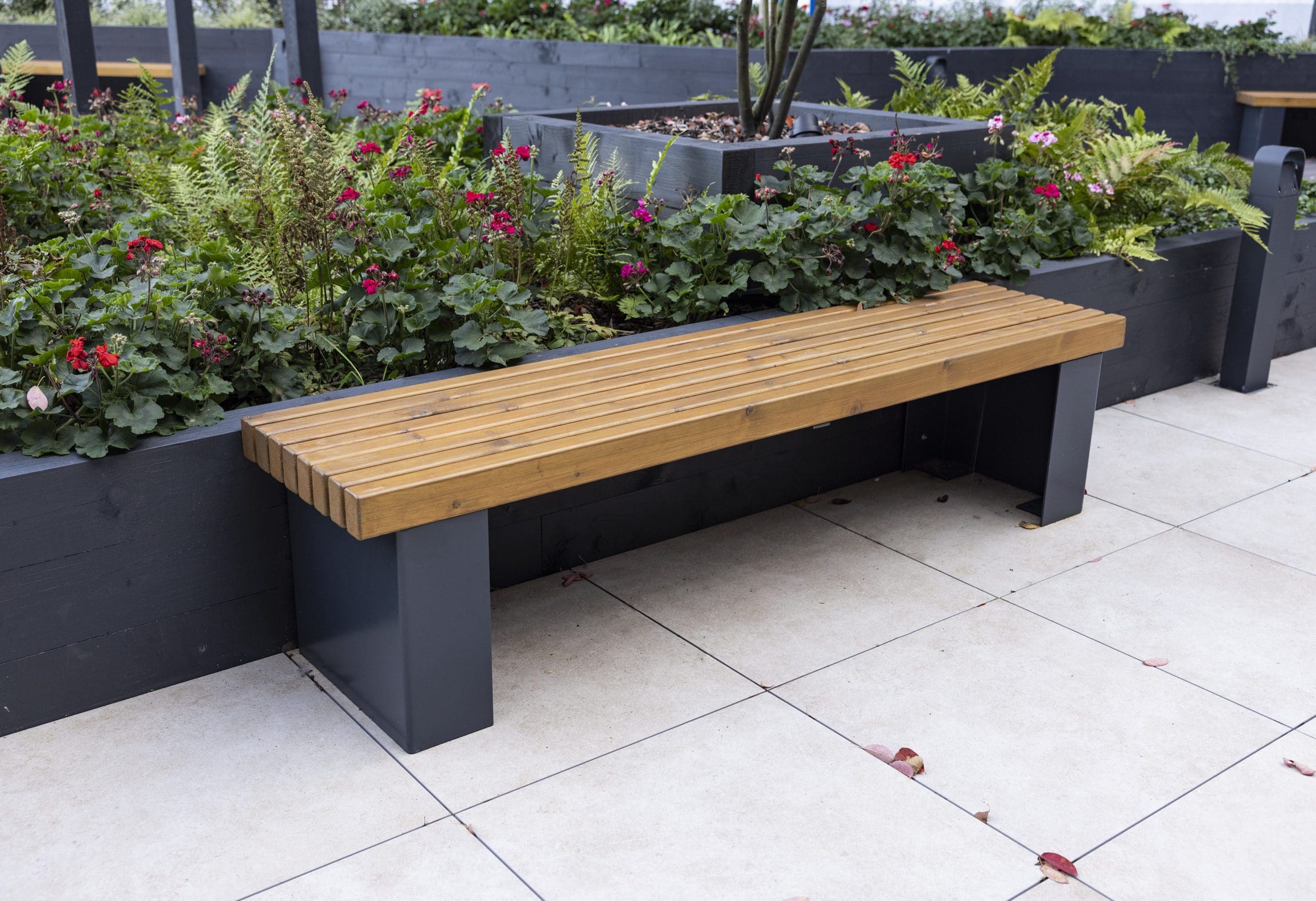 wooden bench with black metal legs infront of plants