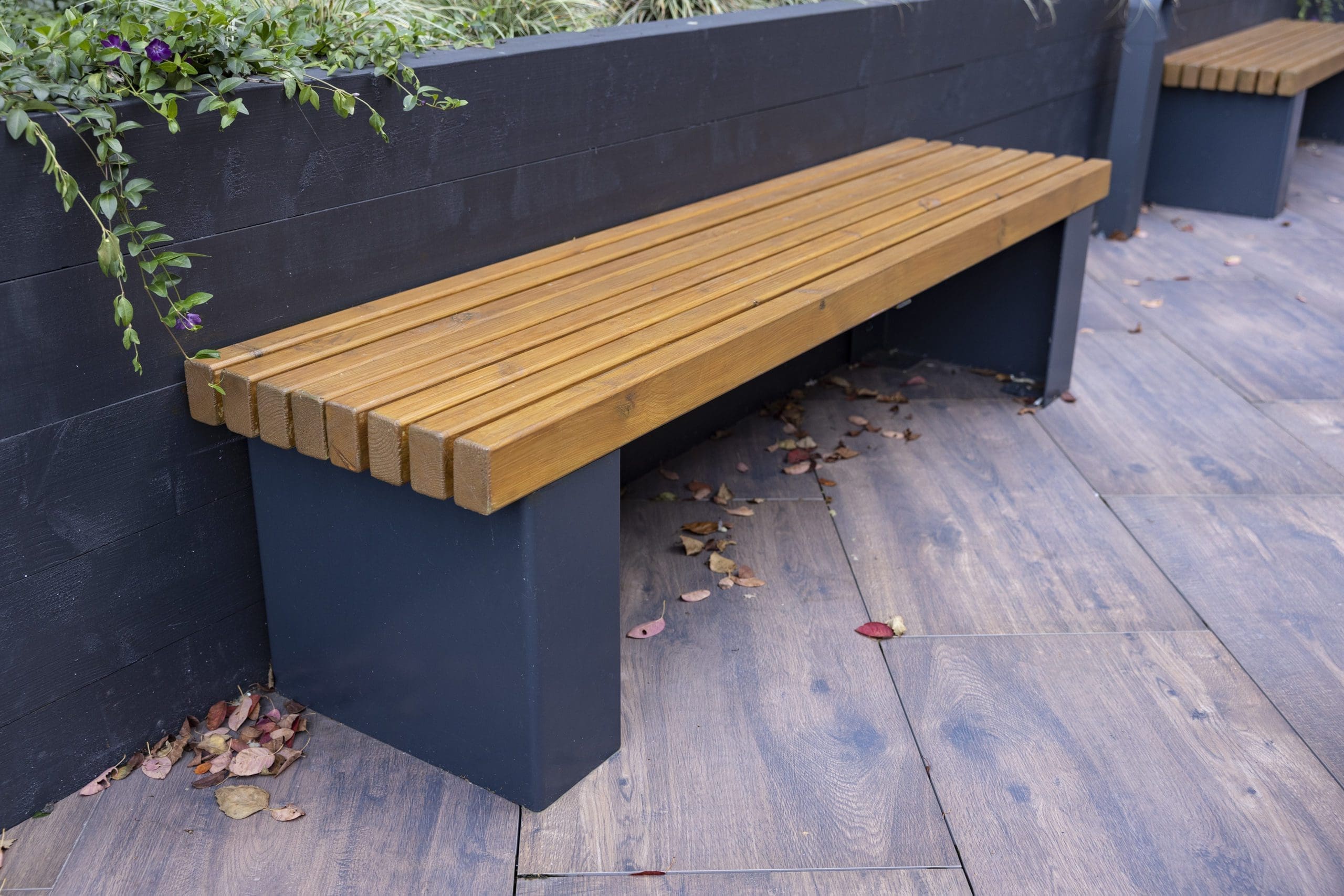 wooden bench with black metal legs infront of plants