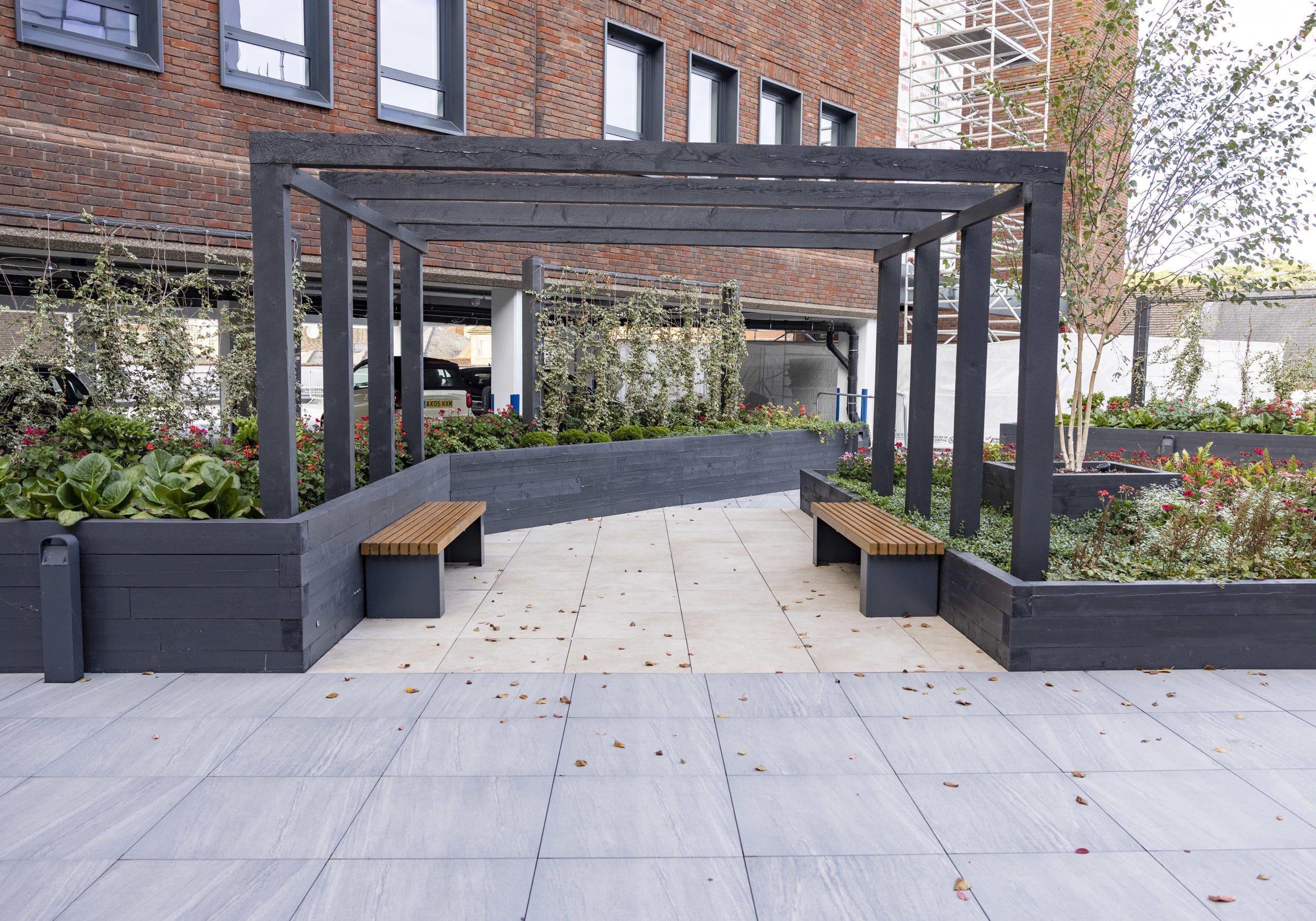 dark blackwooden pergola with matching retaining wall and brown benches with black metal legs