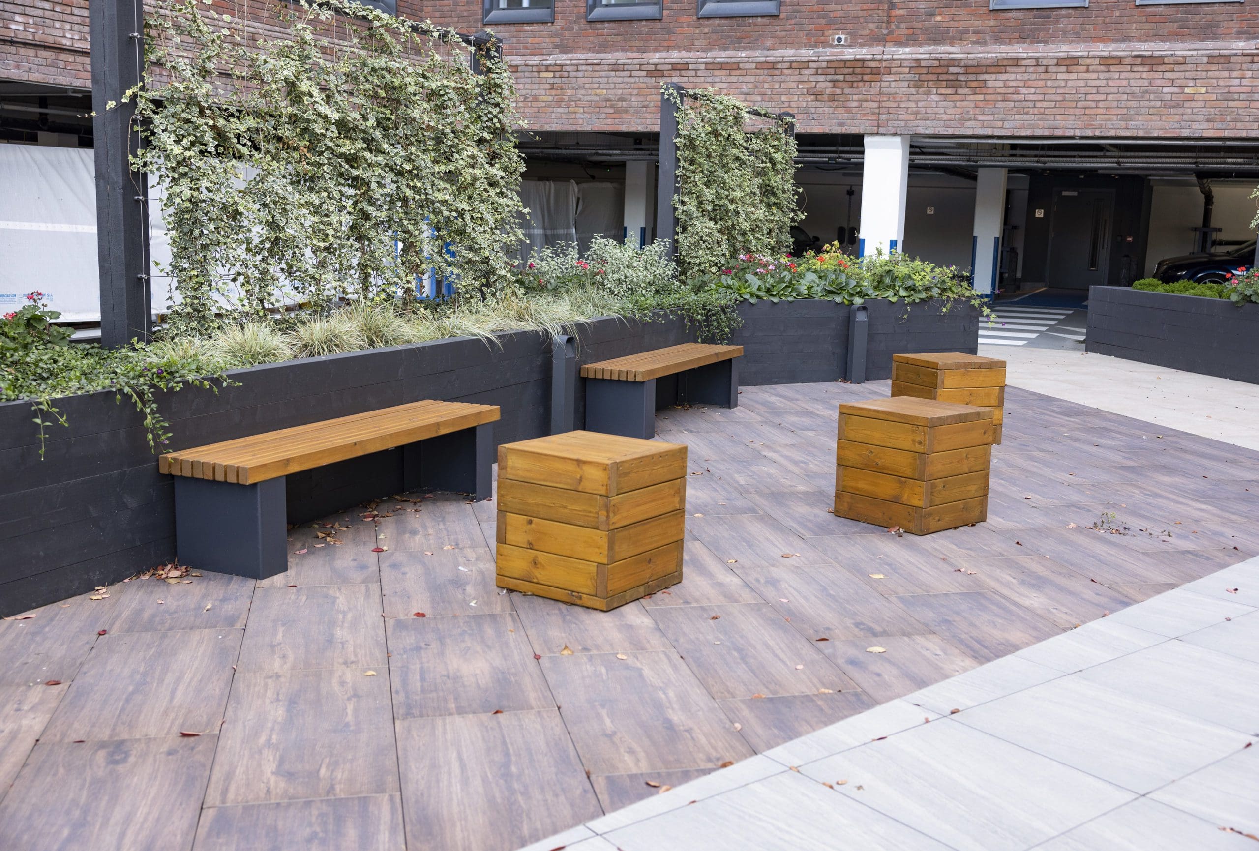 wooden square block individual seats and benches with black metal legs infront of plants