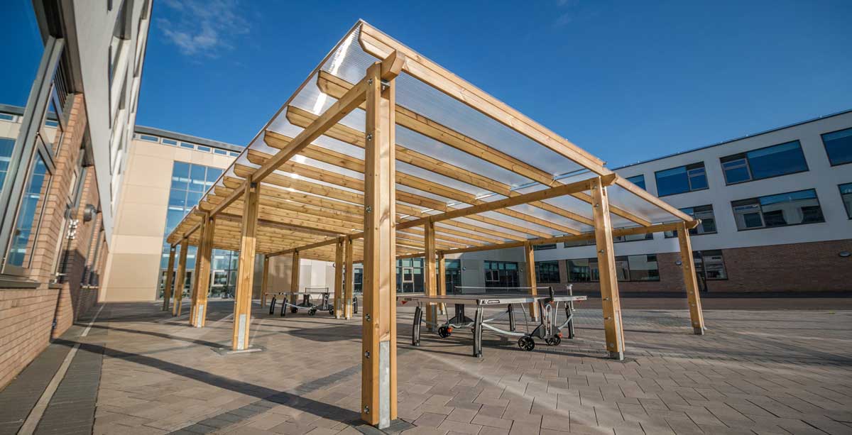Large outdoor wooden pergola covering tablet tennis tables in school courtyard
