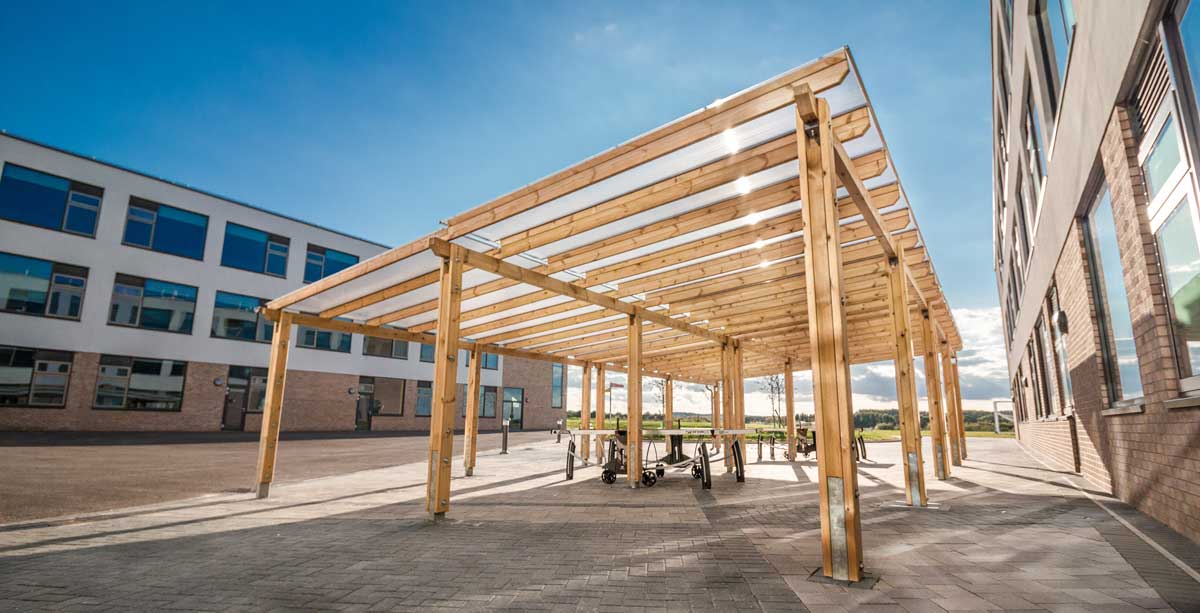 Large outdoor wooden pergola covering tablet tennis tables in school courtyard