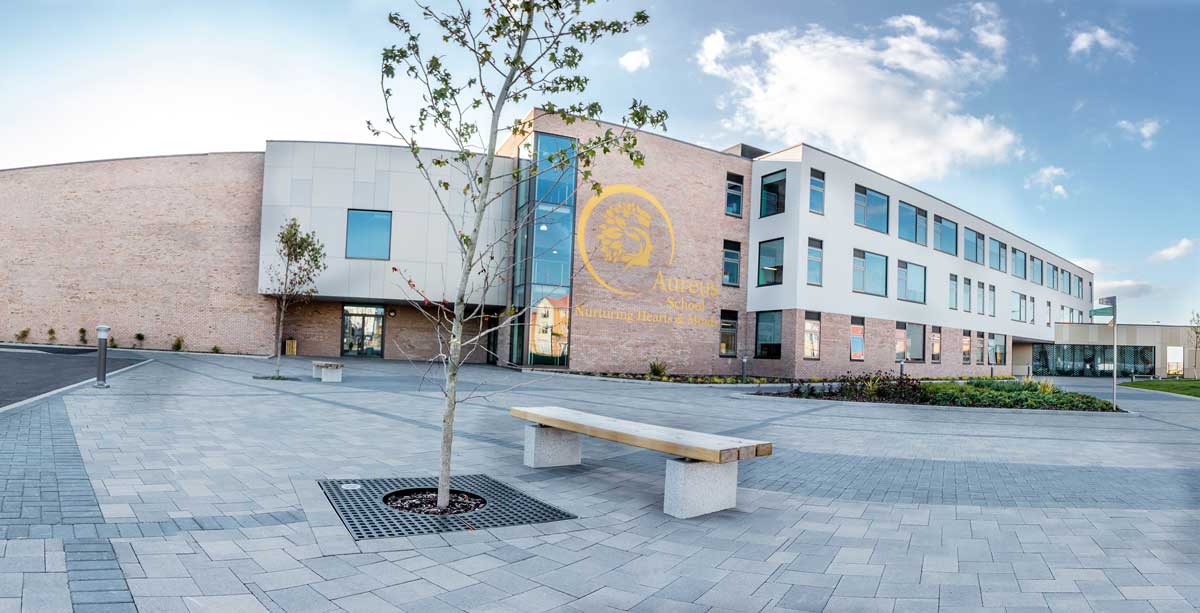 Exterior wide shot of school showing wooden bench with concrete plinth legs infront of tree