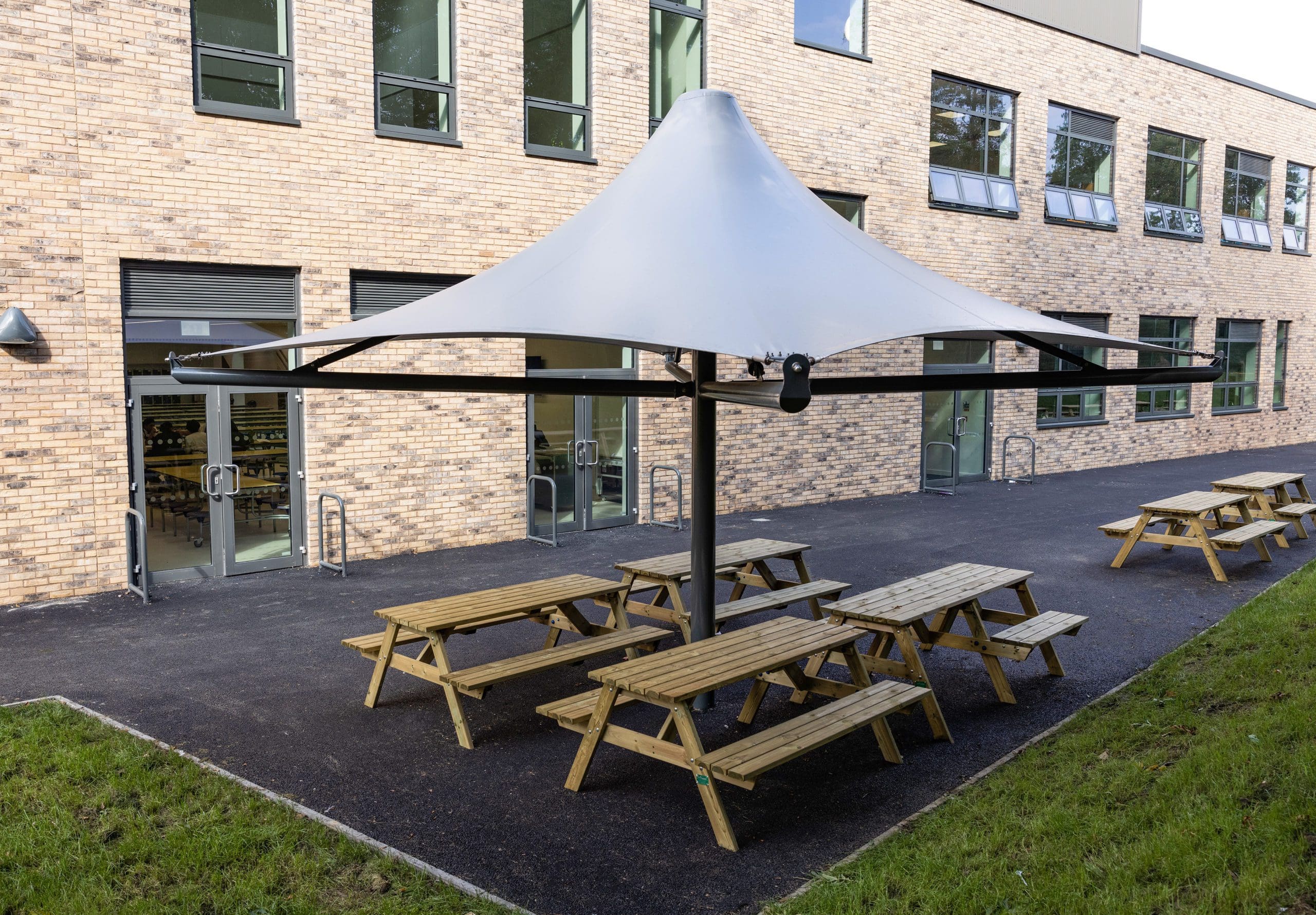 Large outdoor stretch square parasol over 4 wooden picnic tables