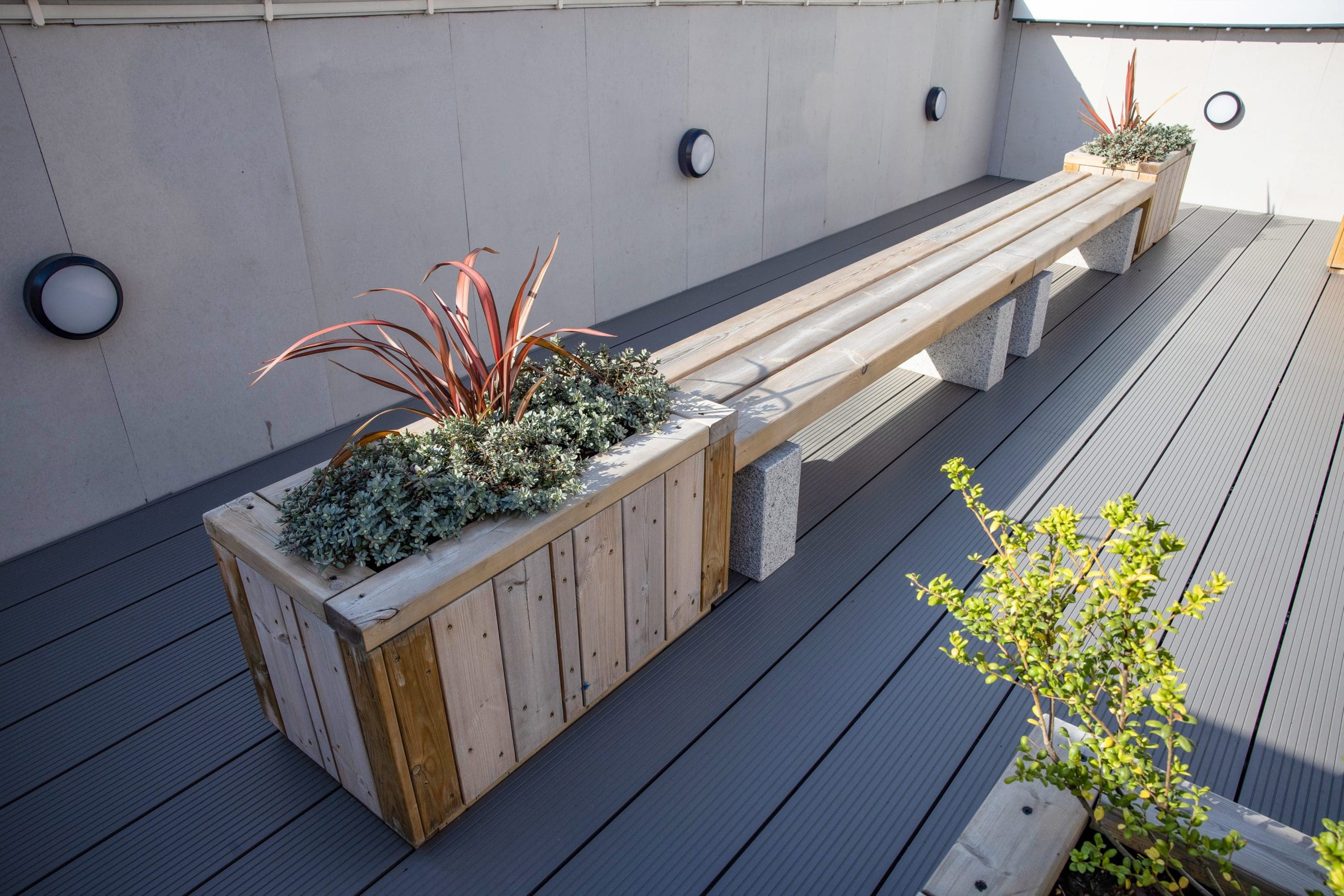 outdoor rooftop wooden planters left and right of wooden bench with concrete plinth legs