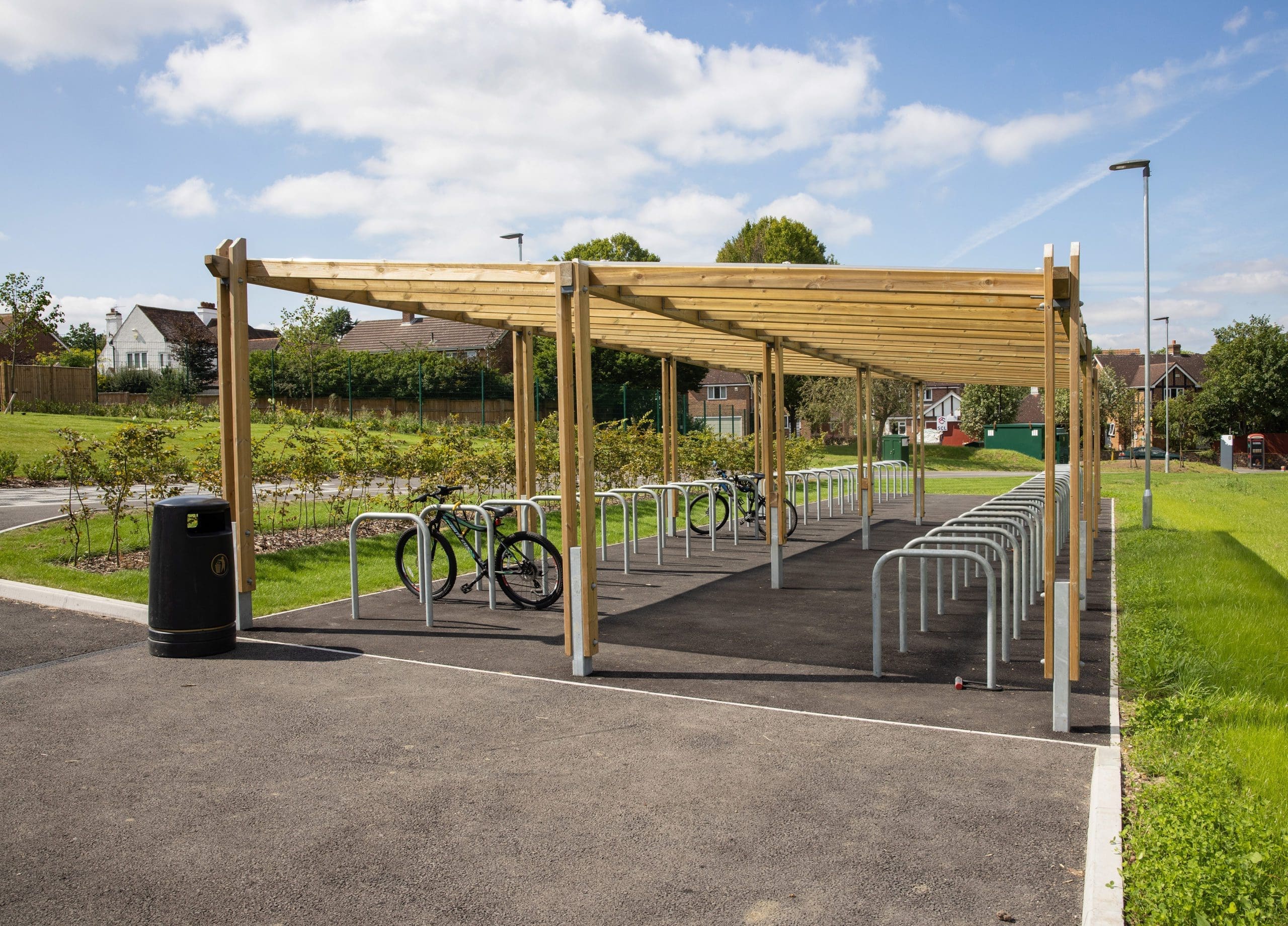 two rows of metal bike lock hoops with half under wooden pergola shelter