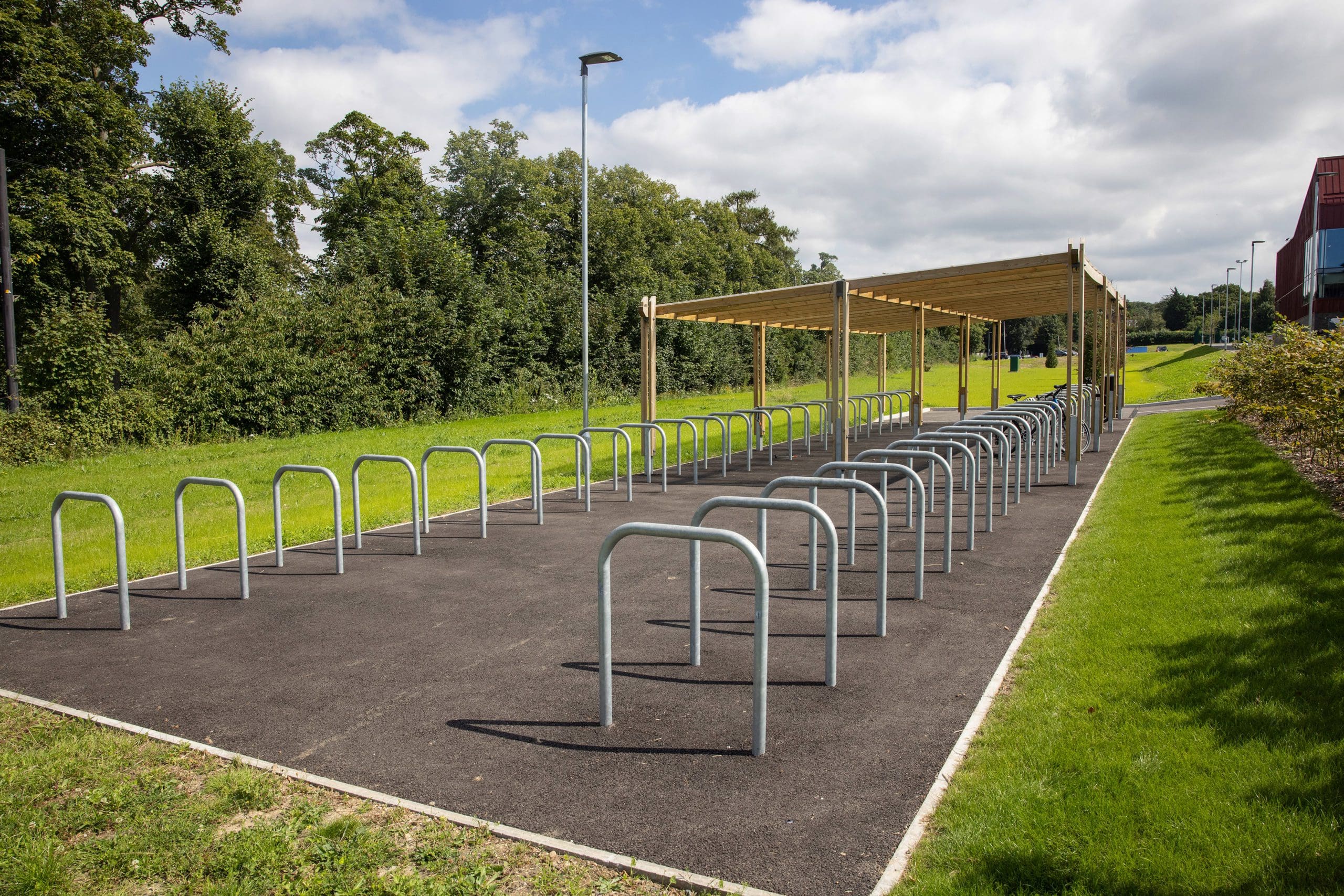 two rows of metal bike lock hoops with half under wooden pergola shelter