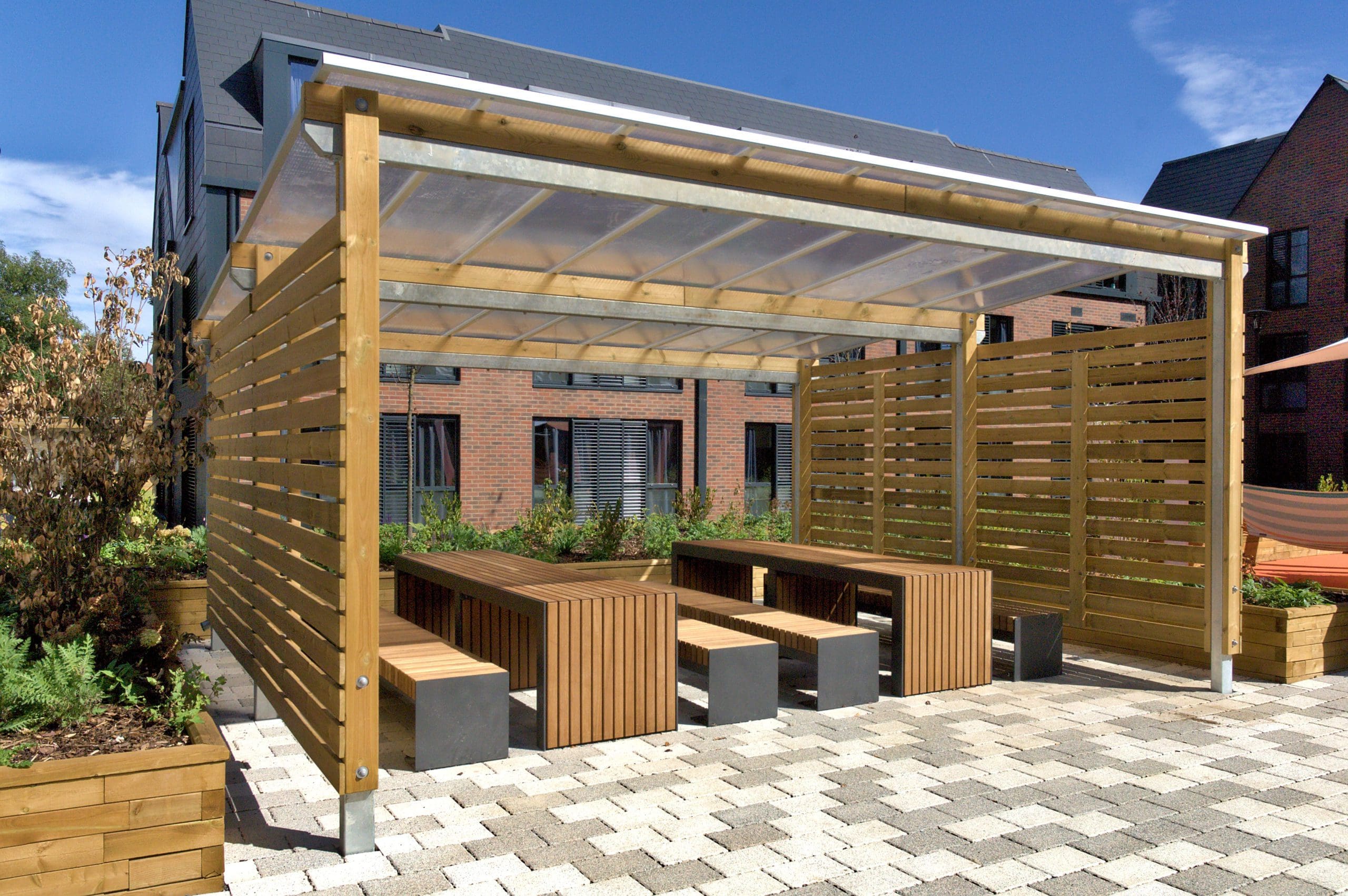 Outdoor canopy with wooden sides and see through plastic top covering a variety of wooden picnic tables and benches