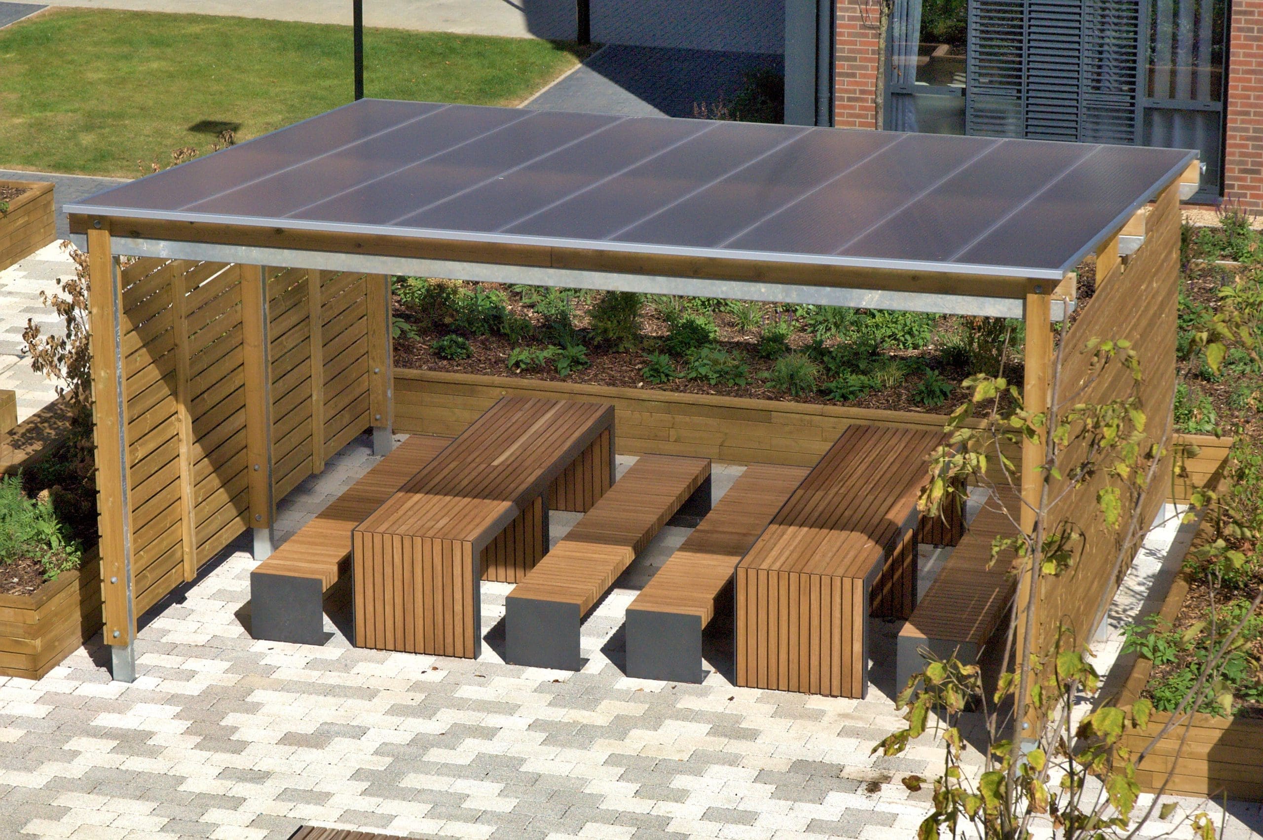Outdoor canopy with wooden sides and see through plastic top covering a variety of wooden picnic tables and benches