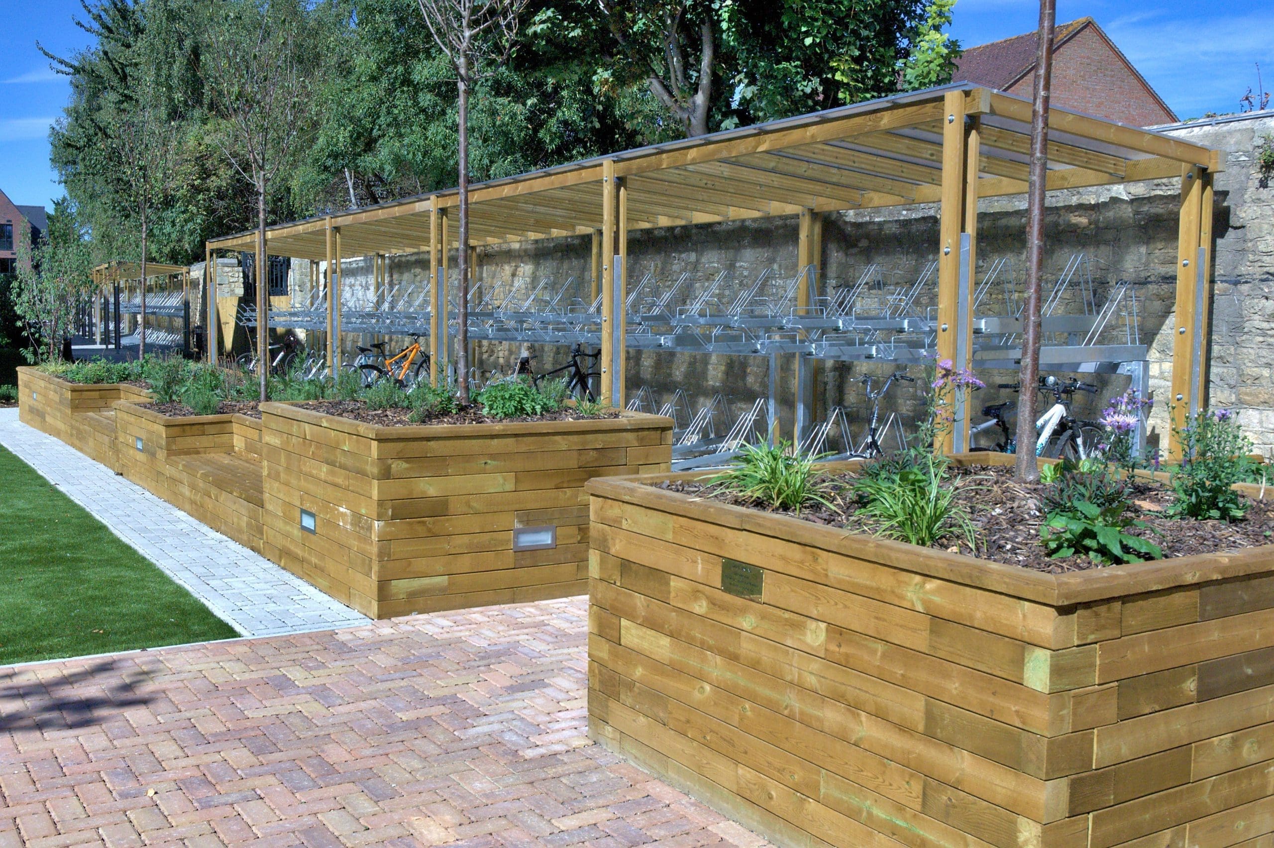 Long outdoor canopy with wooden sides and see through plastic top covering metal two tiered bicycle stores
