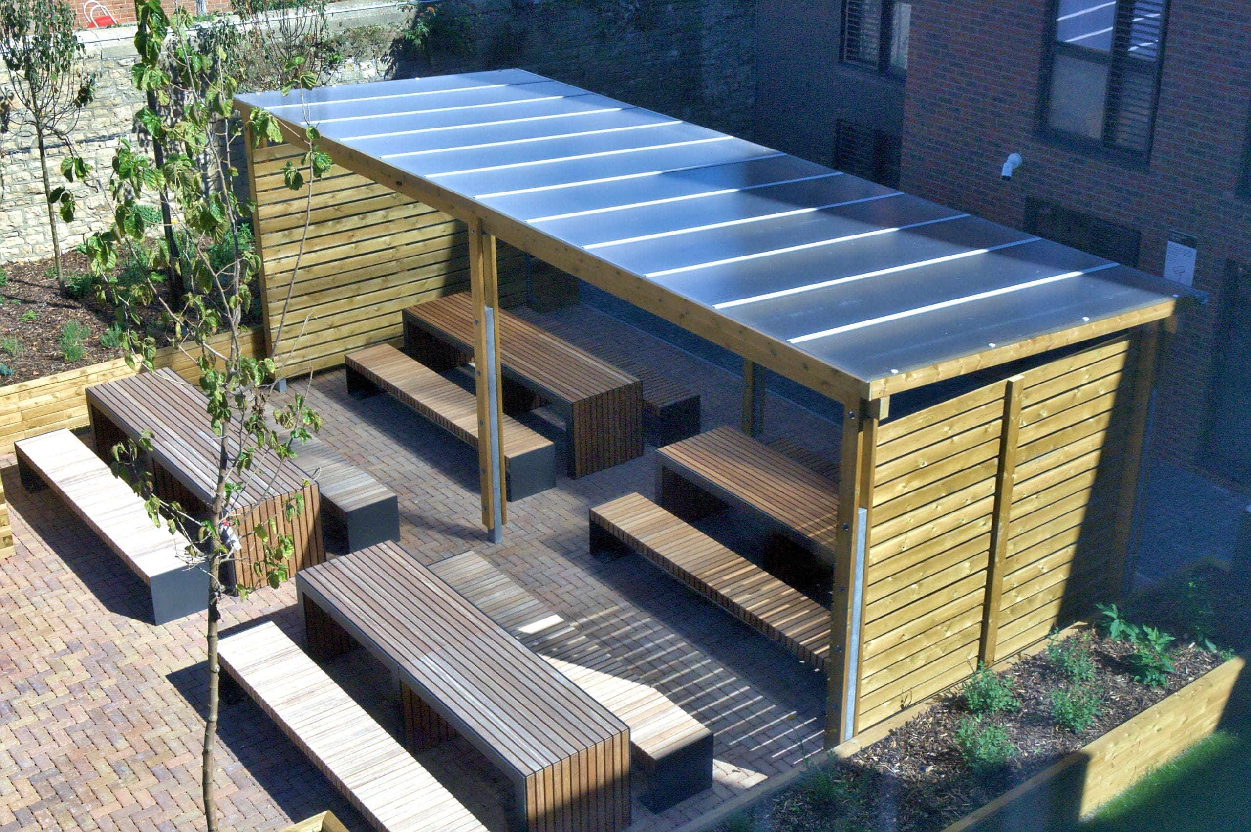 Outdoor canopy with wooden sides and see through plastic top covering a variety of wooden picnic tables and benches