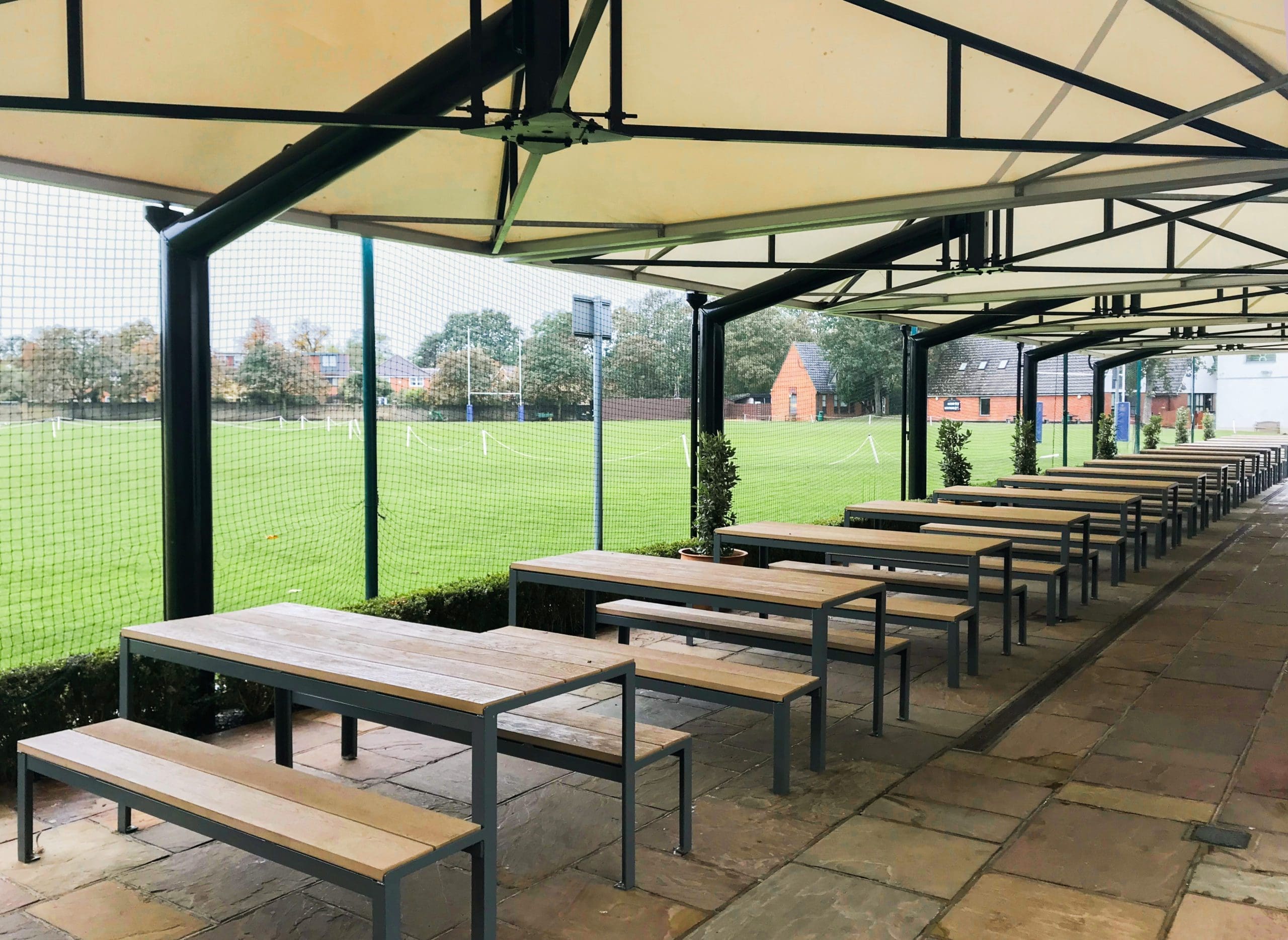 long line of wooden and metal picnic tables with matching benches under long outdoor metal and fabric canopy
