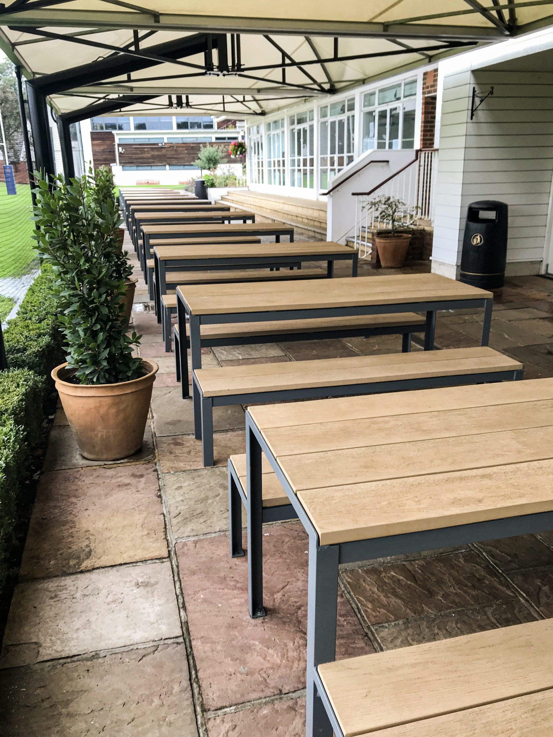 long line of wooden and metal picnic tables with matching benches under long outdoor metal and fabric canopy