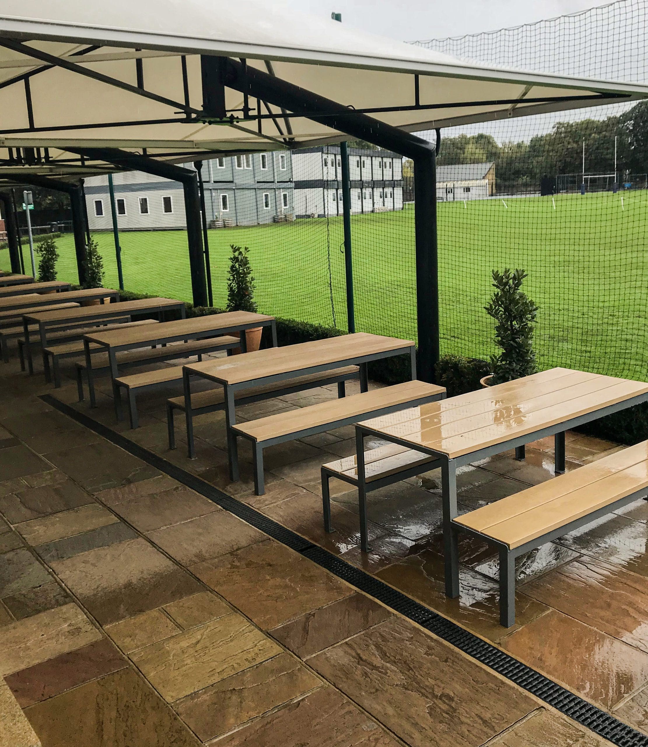 long line of wooden and metal picnic tables with matching benches under long outdoor metal and fabric canopy