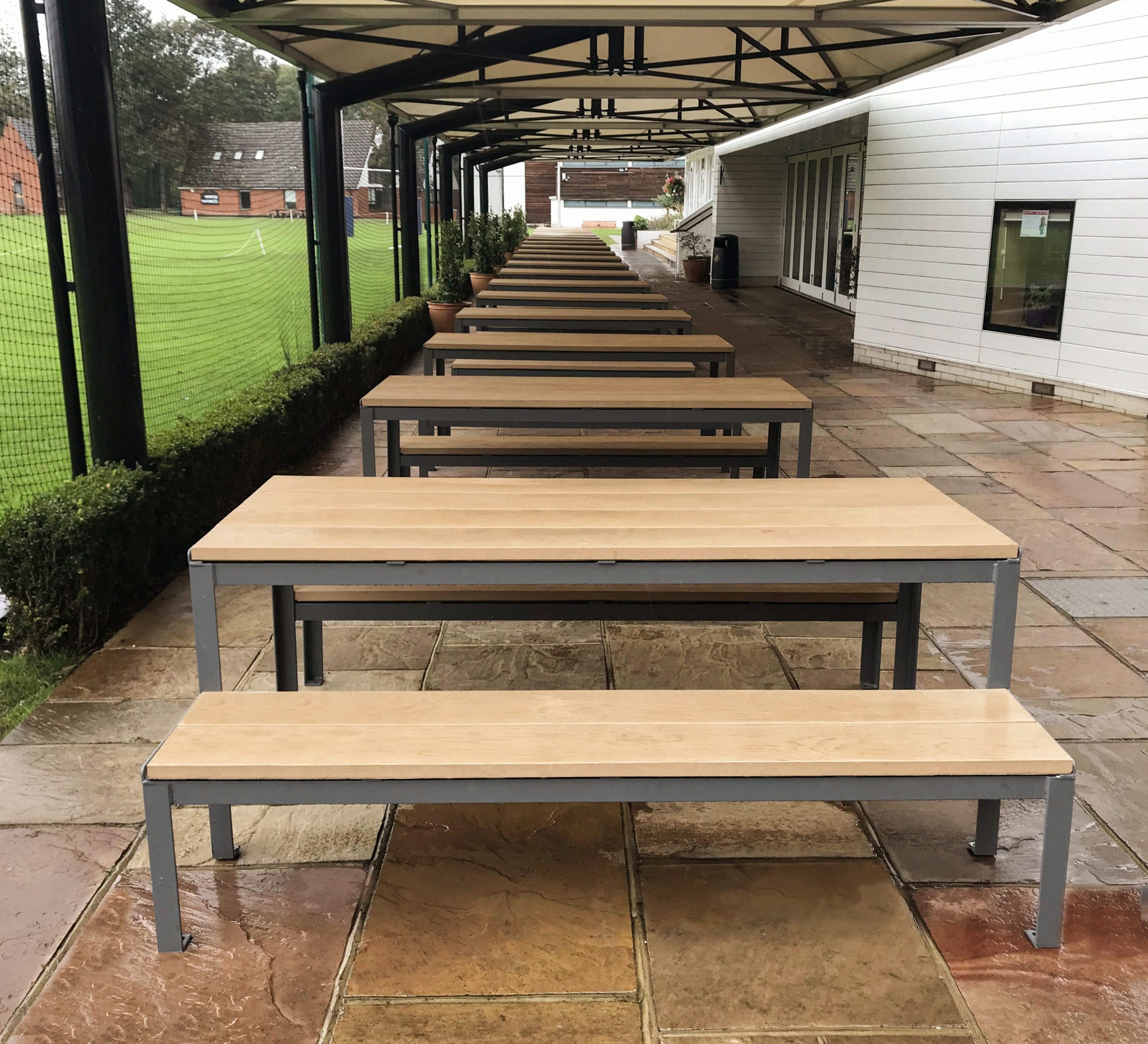 long line of wooden and metal picnic tables with matching benches under long outdoor metal and fabric canopy