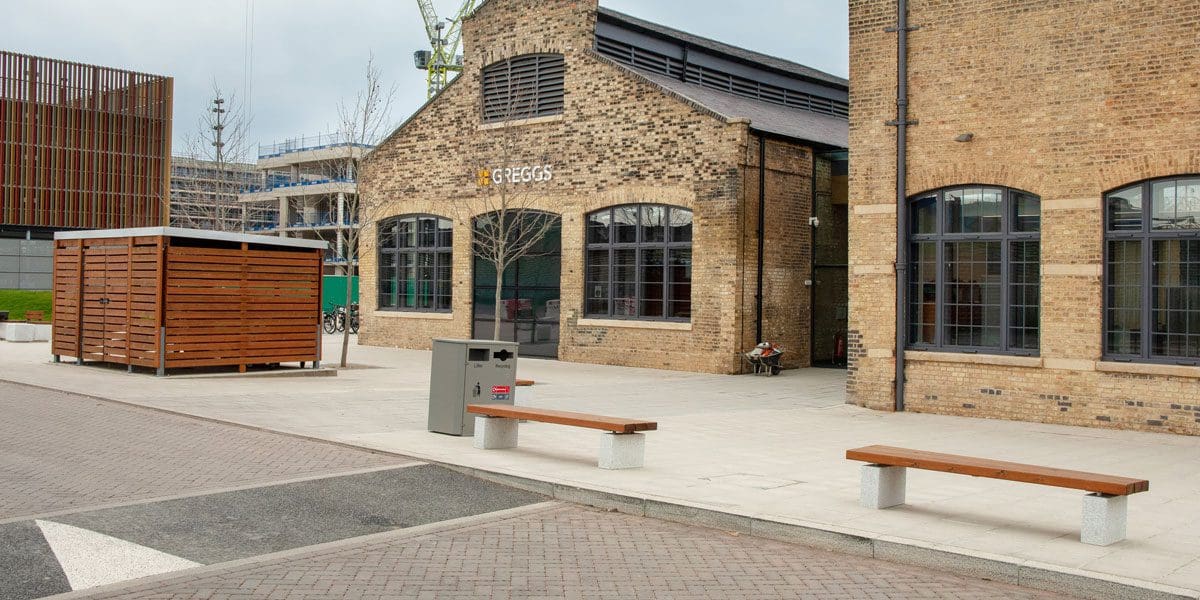 External wooden benches with concrete plinth legs and wooden bin store infront of greggs building