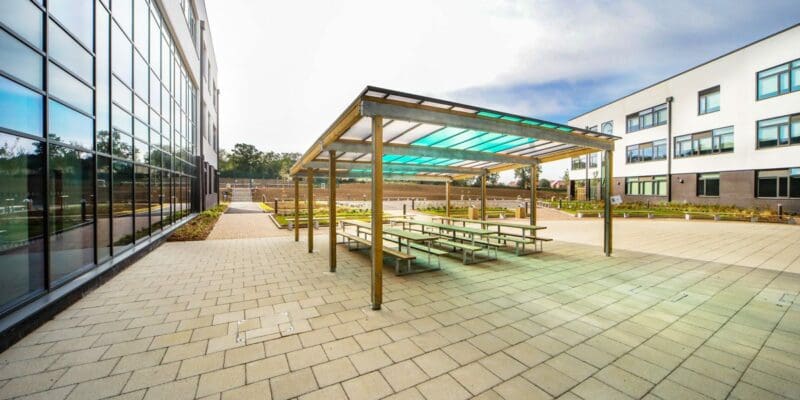 exterior shot of the school showing wooden pergola over outdoor wooden picnic tables and benches