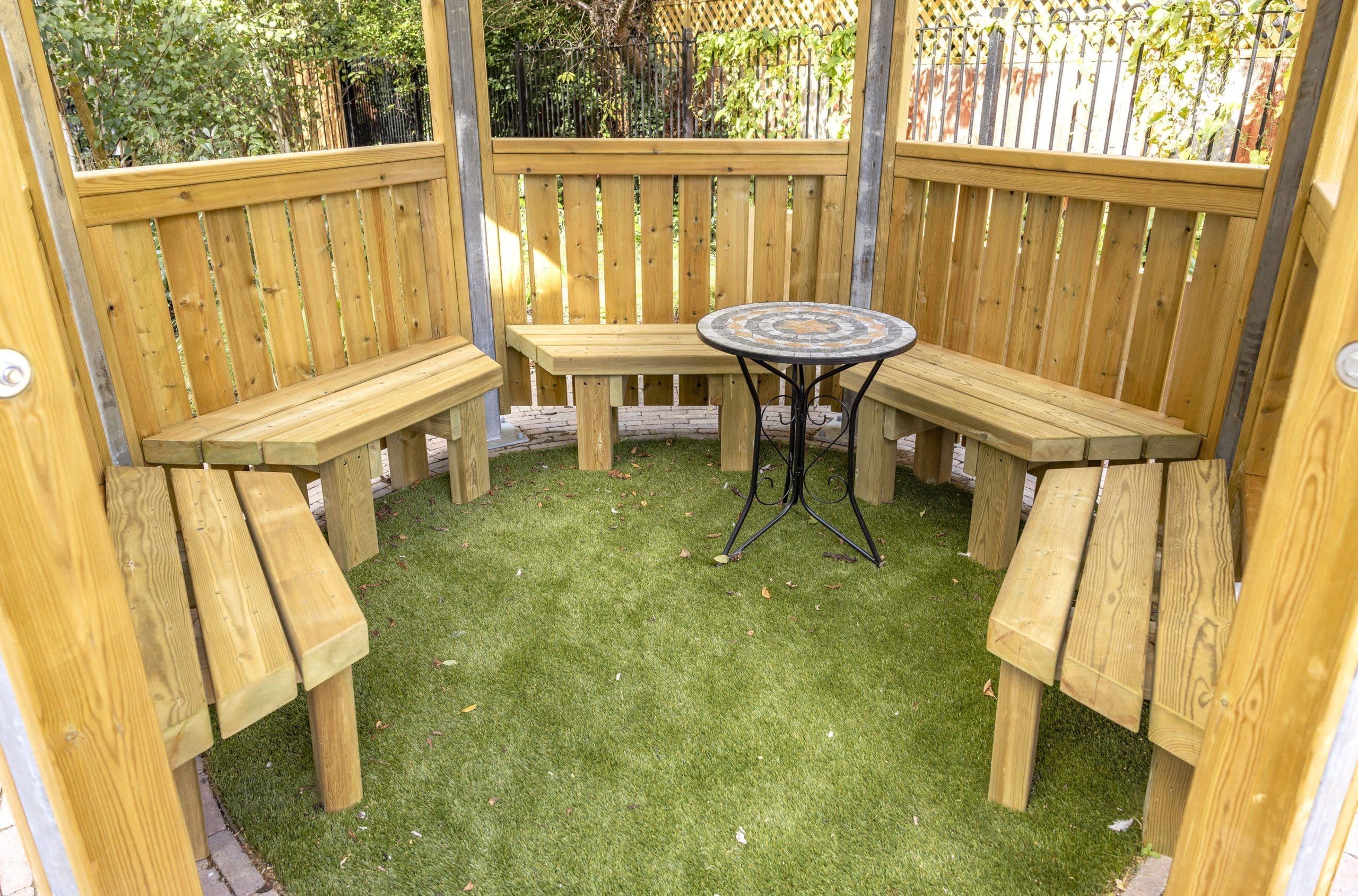 interior of wooden benches attached to hexagonal canopy with metal and tile table
