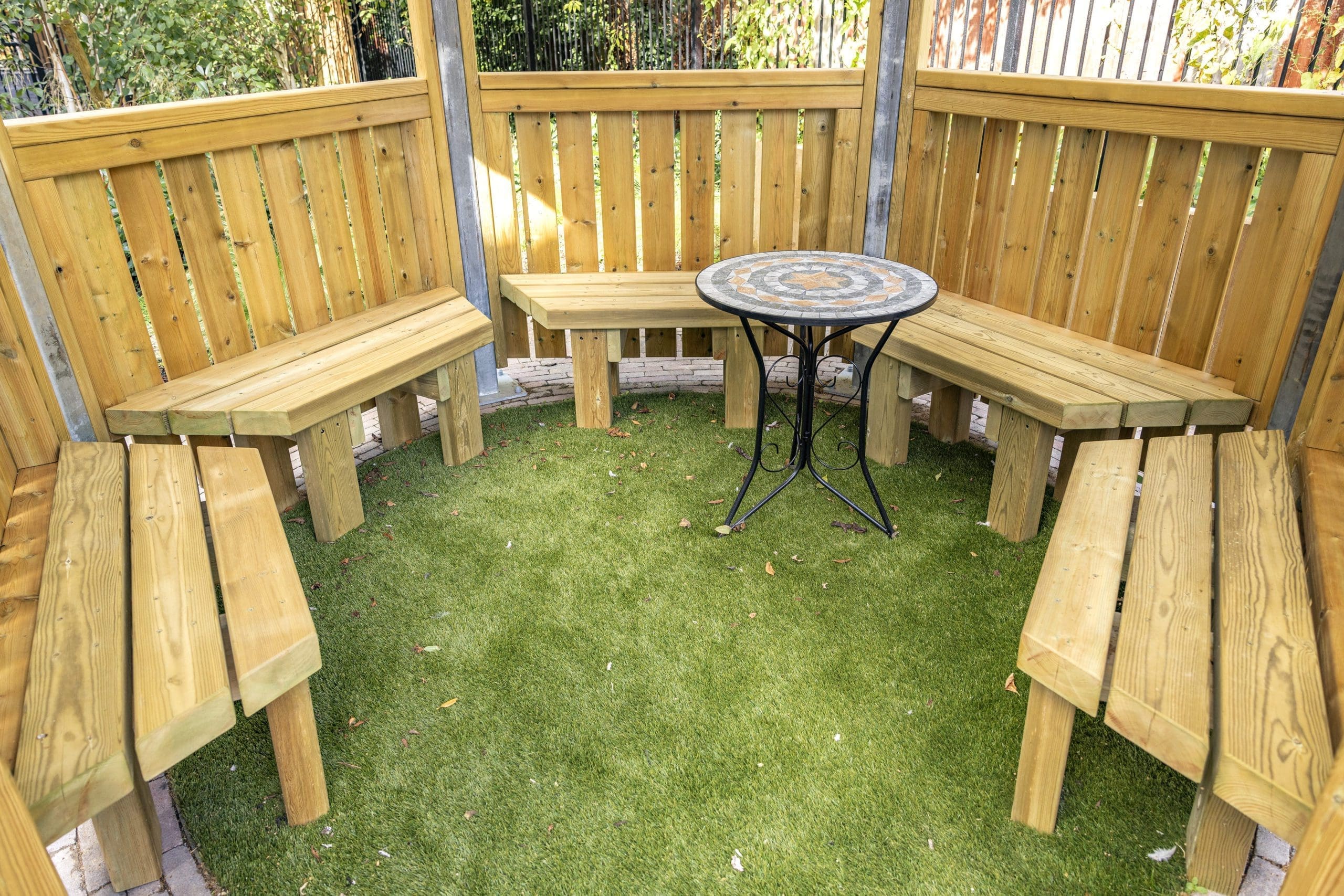 interior of wooden benches attached to hexagonal canopy with metal and tile table