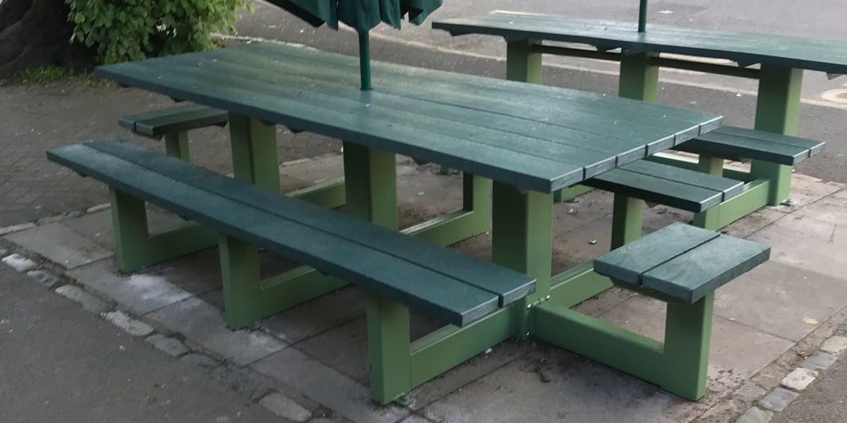 Rows of external plastic green picnic tables with attached bench seats and parasols