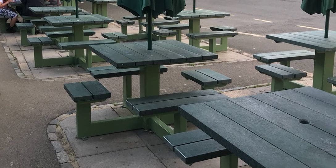 Rows of external plastic green picnic tables with attached bench seats and parasols