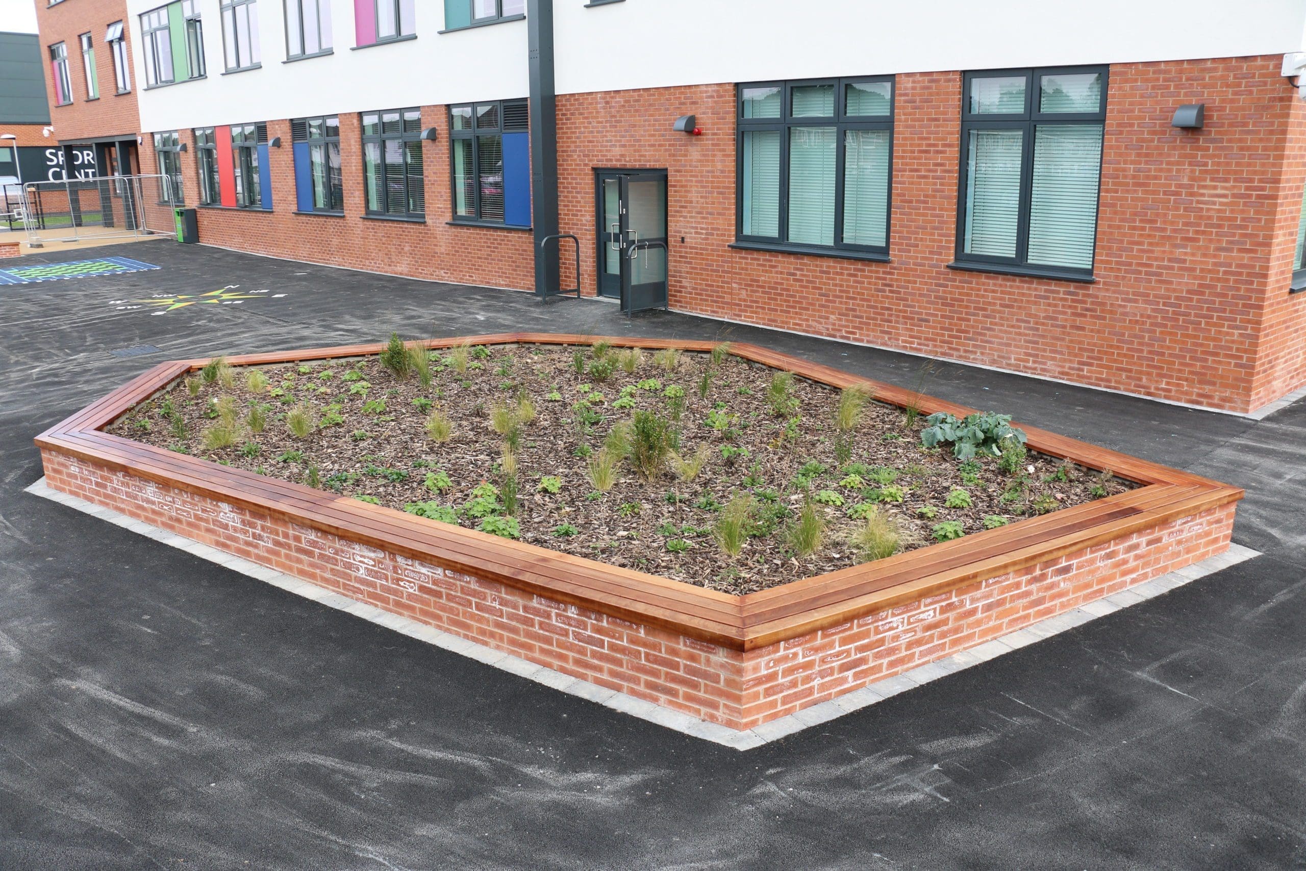 Exterior large hexagonal planted area surrounded by brick wall with wooden seating tops