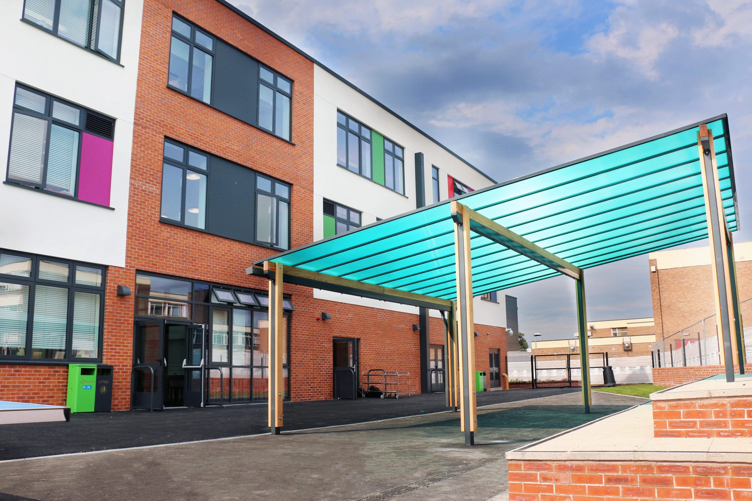 Exterior shot of school showing large wooden pergola with bright blue canopy cover