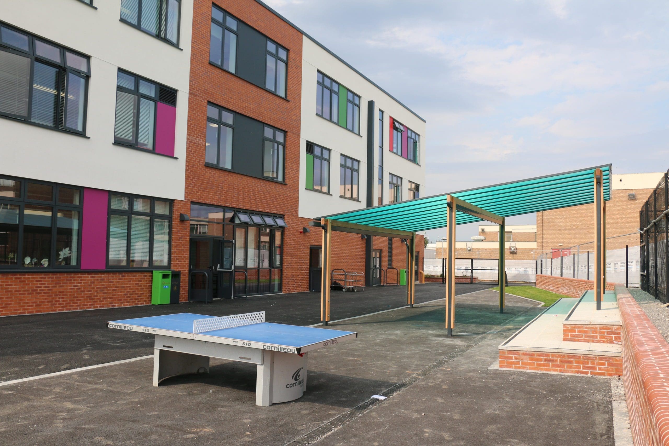 Exterior shot of school showing table tennis table and large wooden pergola with bright blue canopy cover