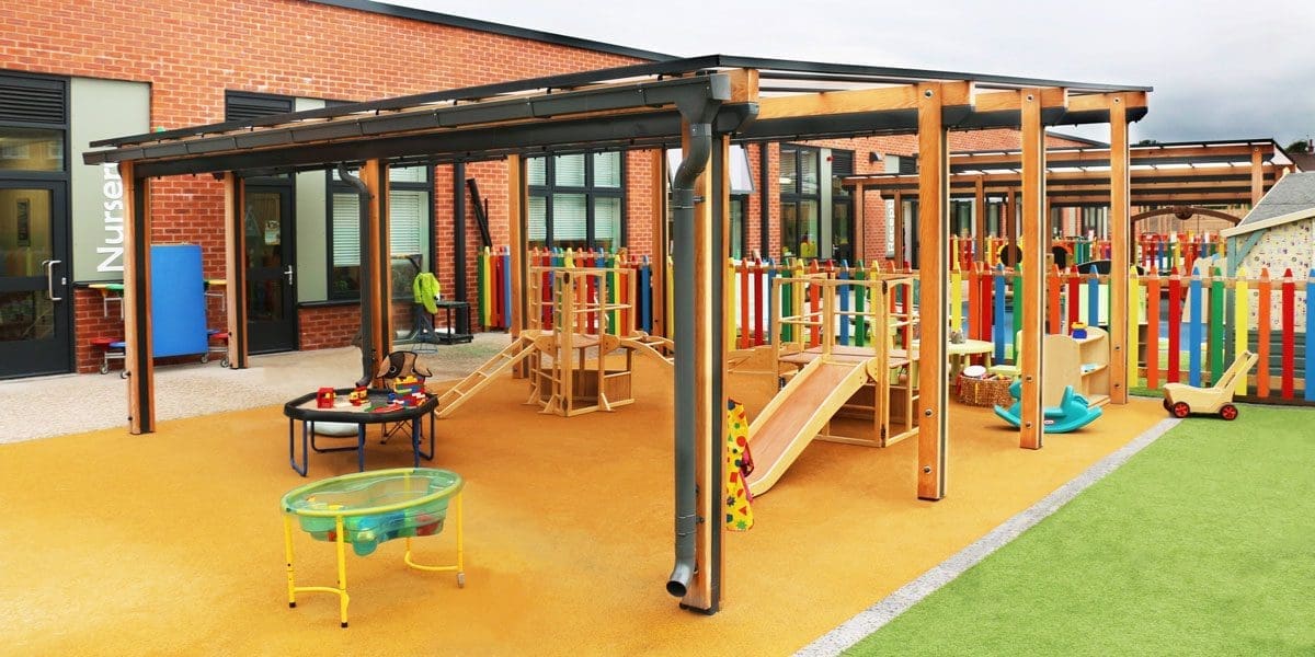 Wooden pergola canopy with black trim and seethrough rood covering colour childrens playground