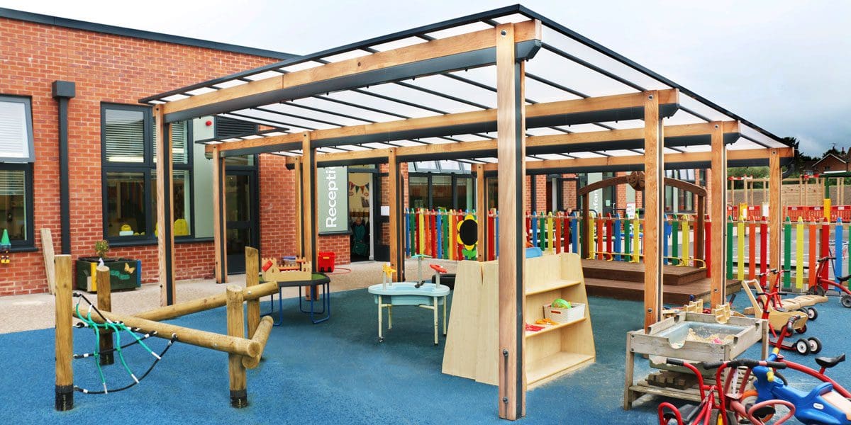 Wooden pergola canopy with black trim and seethrough rood covering colour childrens playground