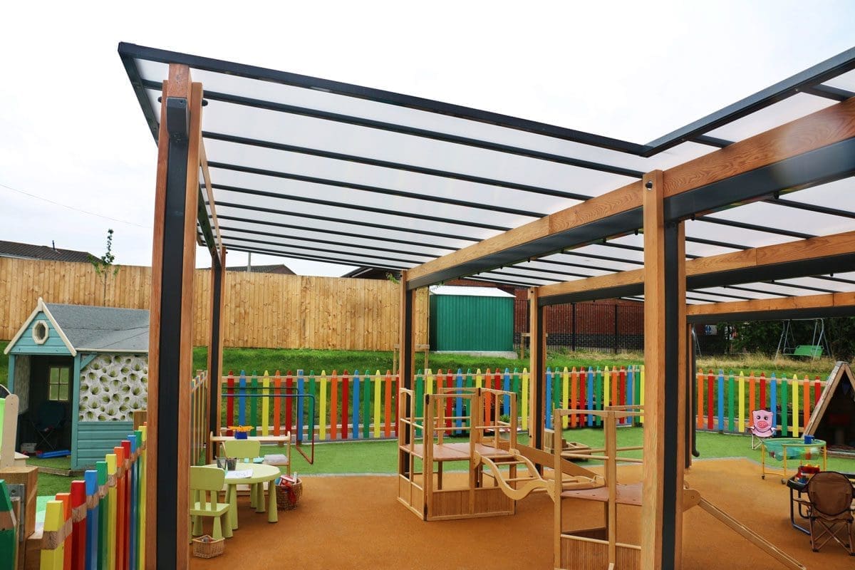 Wooden pergola canopy with black trim and seethrough rood covering colour childrens playground