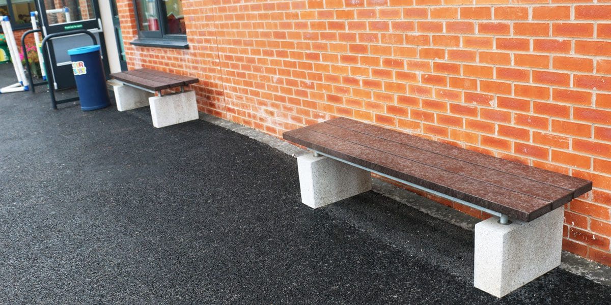 Outdoor wooden benches with concrete plinth legs against wall