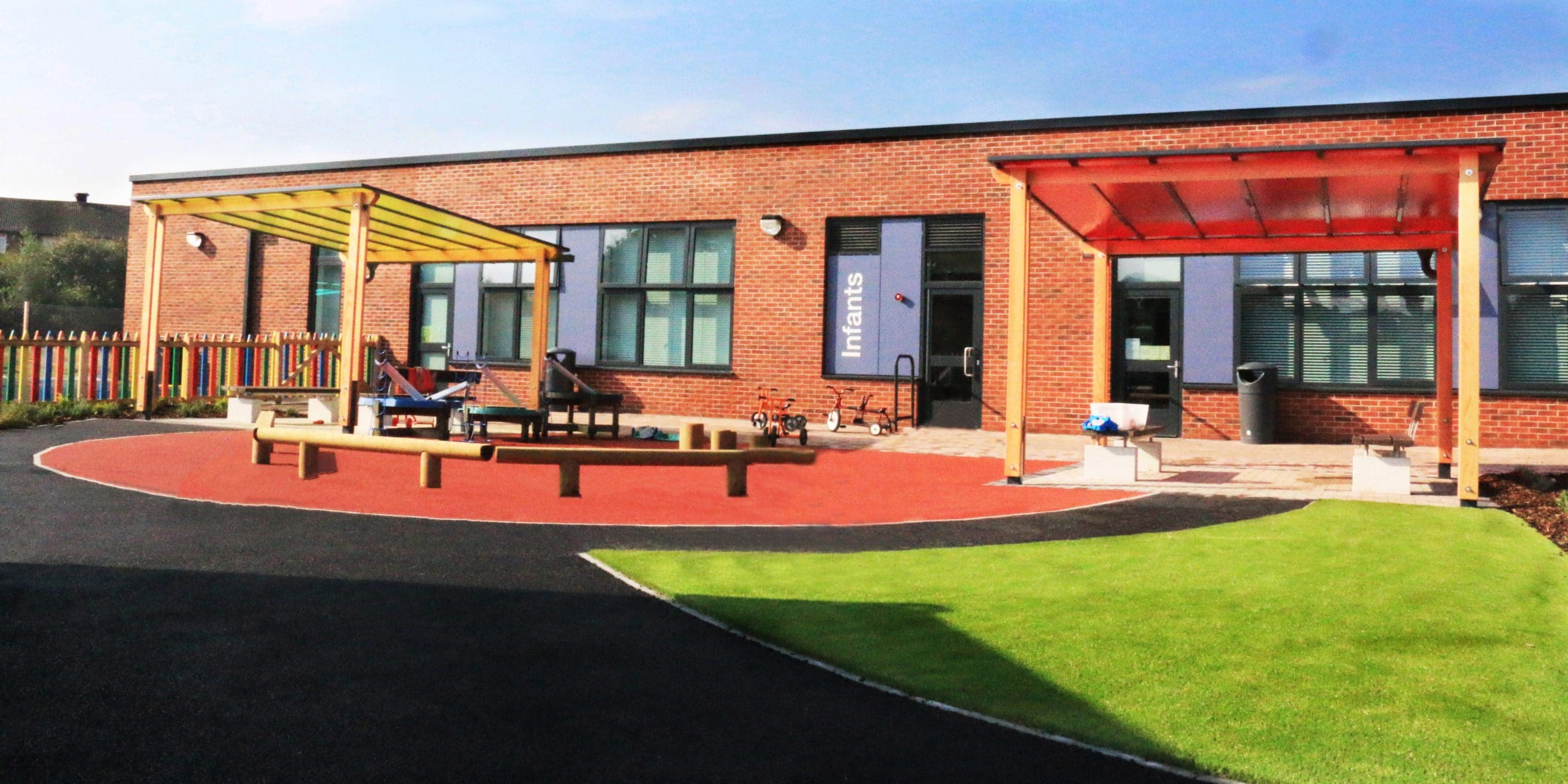 2 external pergolas, one with red and one with yellow tinted canopy colours infront on red coloured tarmac playground