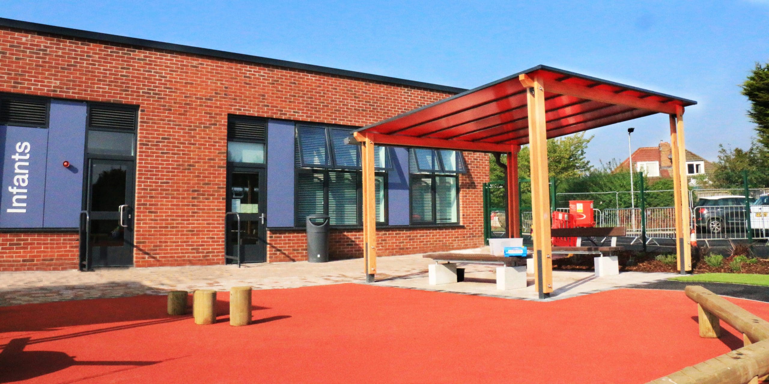 External pergola with red tinted canopy colour infront on red coloured tarmac playground