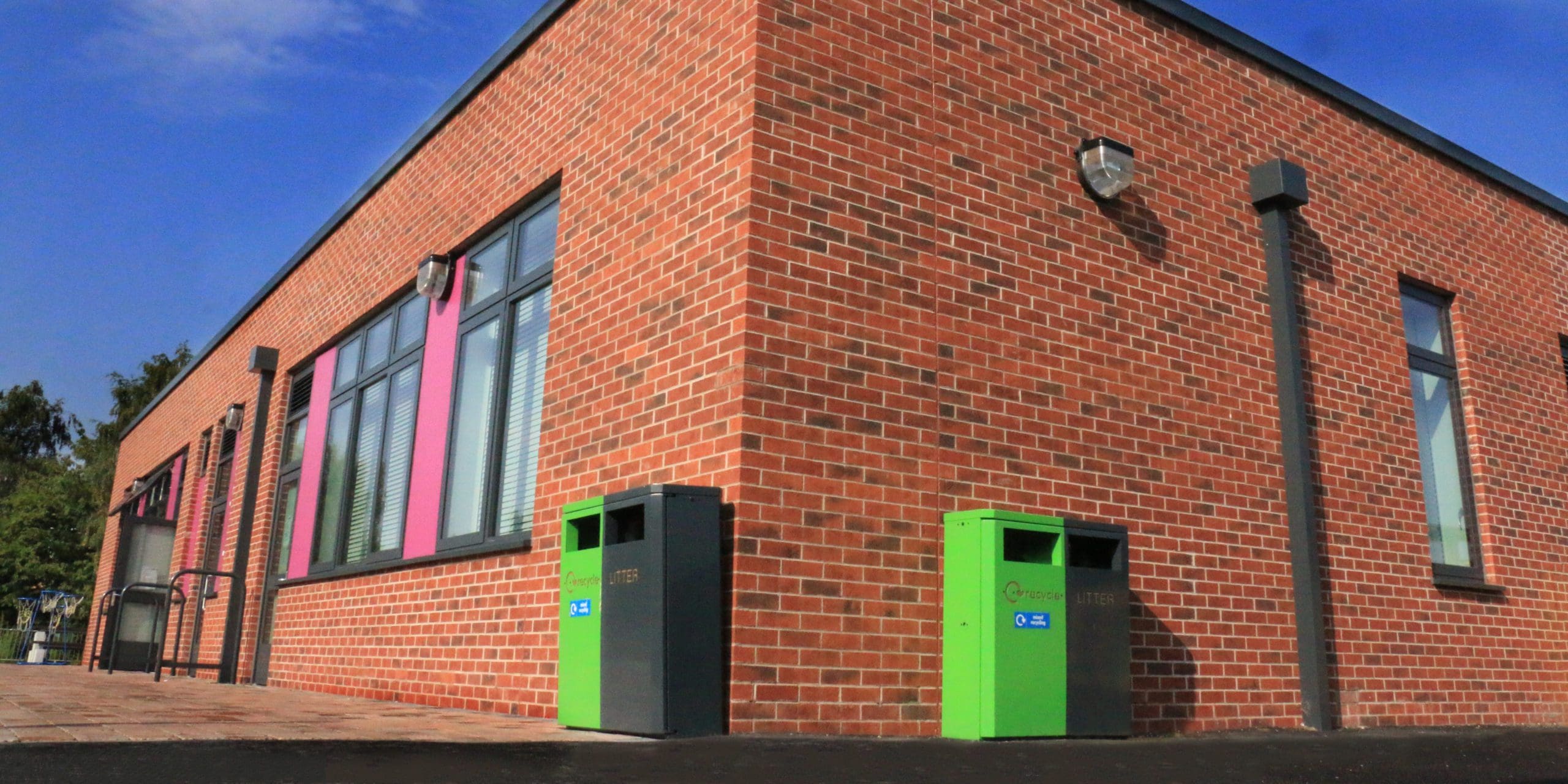corner of school building showing outdoor split green and black metal bins for rubbish and recycling