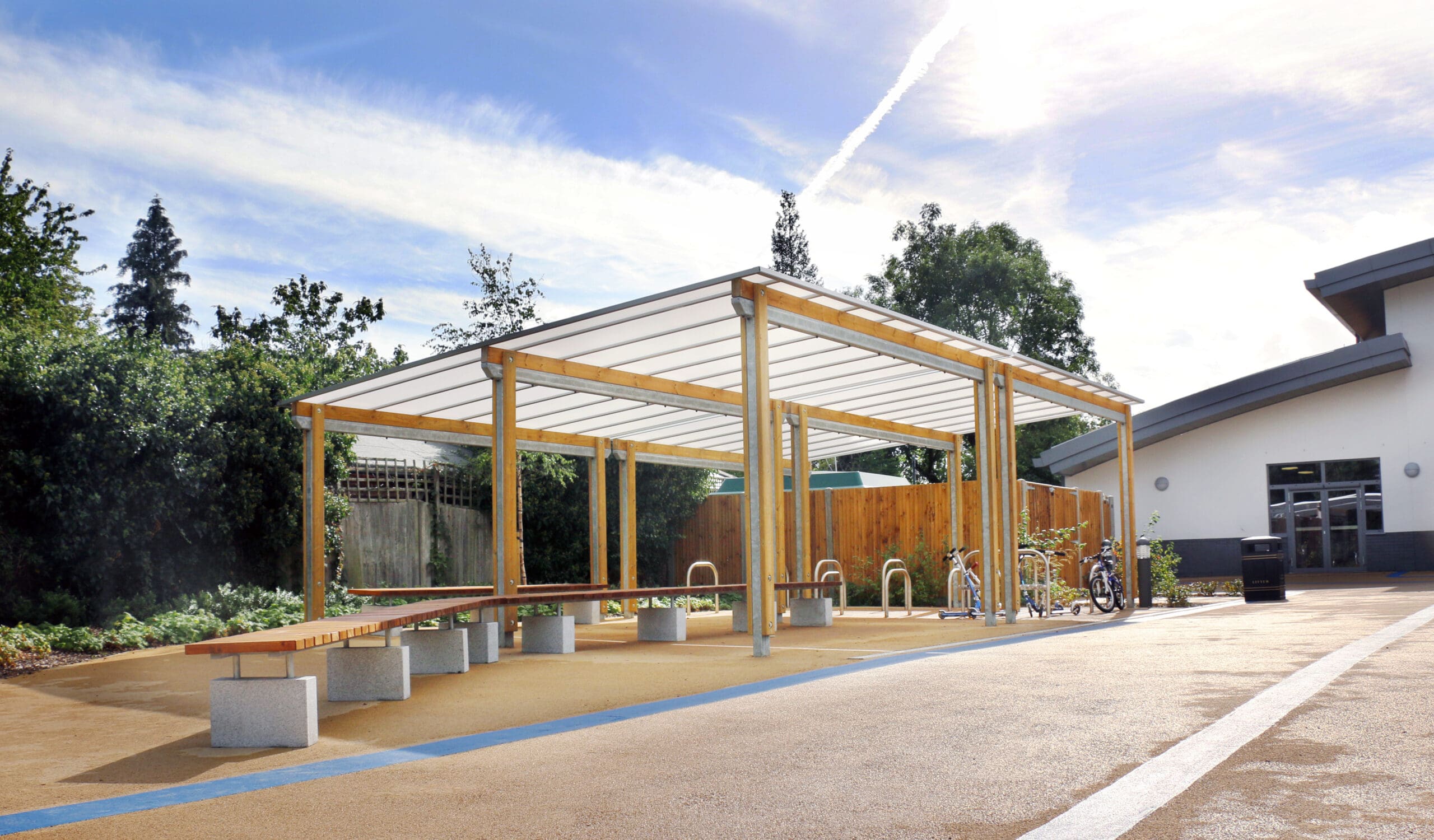 Large pergola with canopy covering bicycle and scooter parking racks and wooden benches with concrete plinth legs