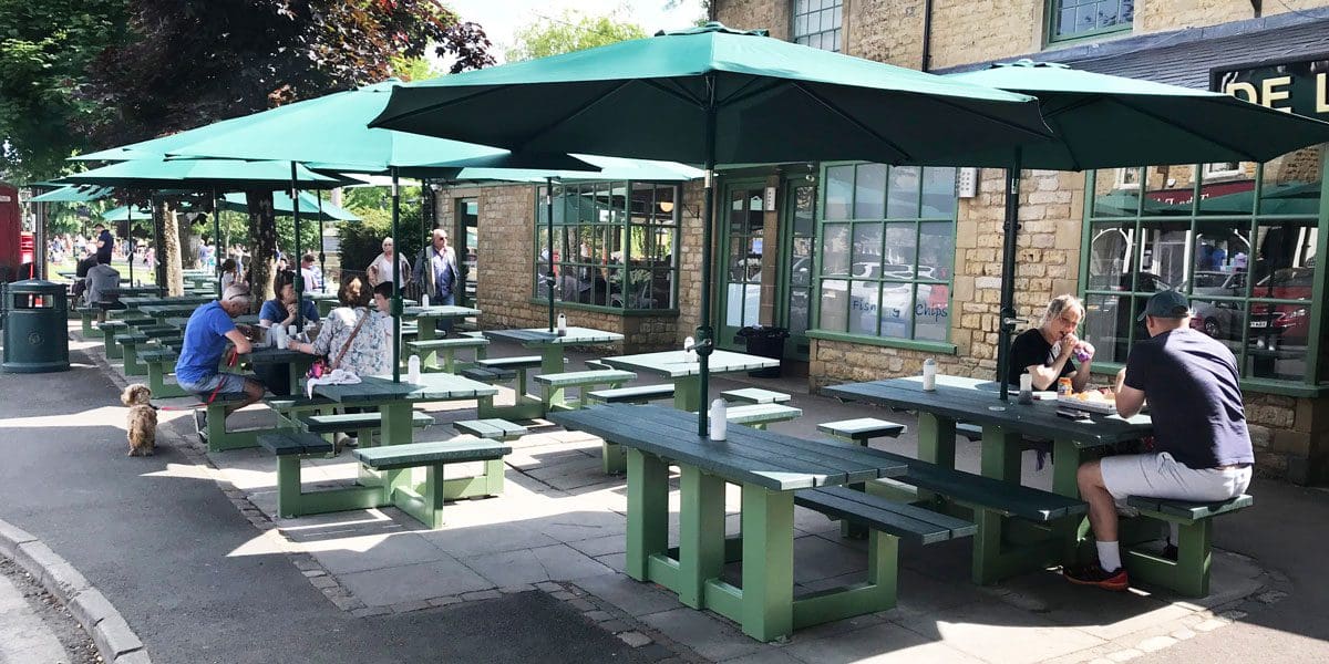 Rows of external plastic green picnic tables with attached bench seats and parasols