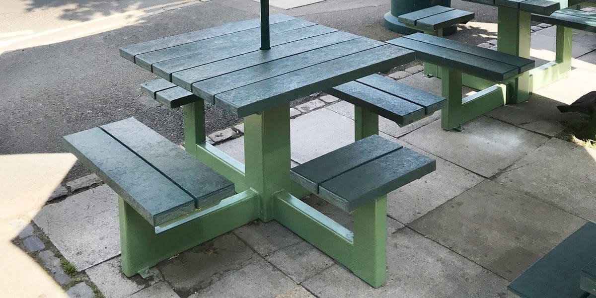 Rows of external plastic green picnic tables with attached bench seats and parasols