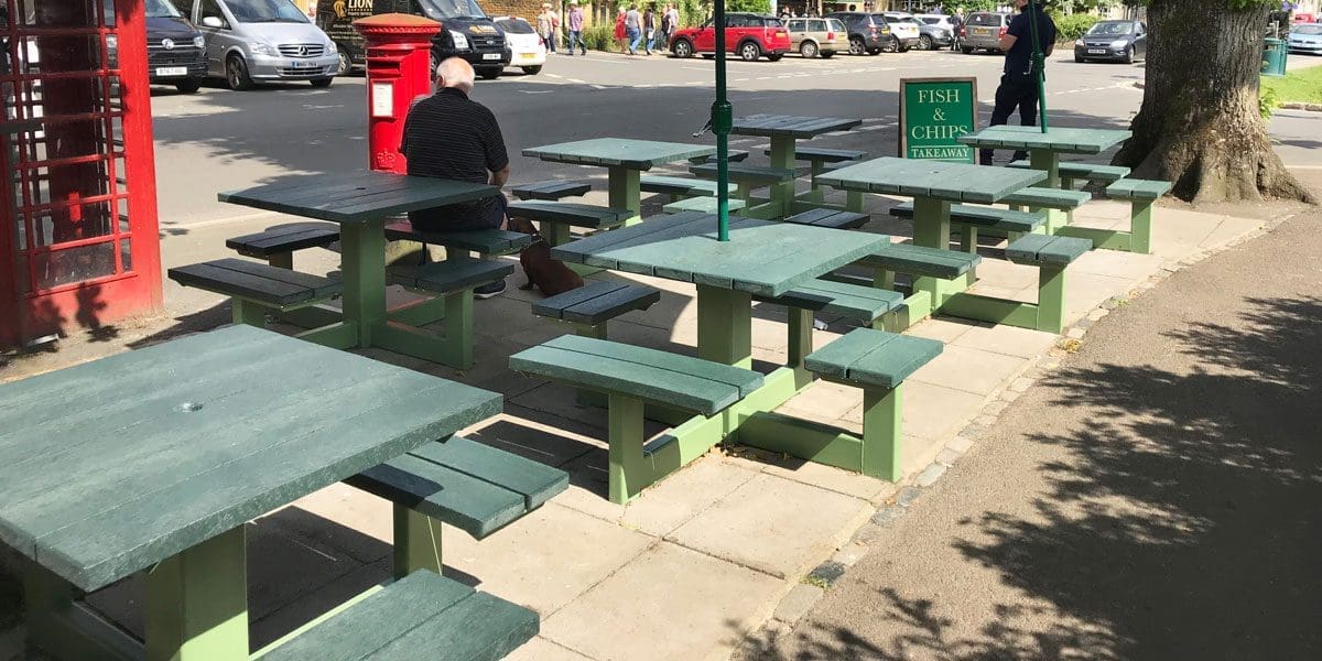 Rows of external plastic green picnic tables with attached bench seats and parasols