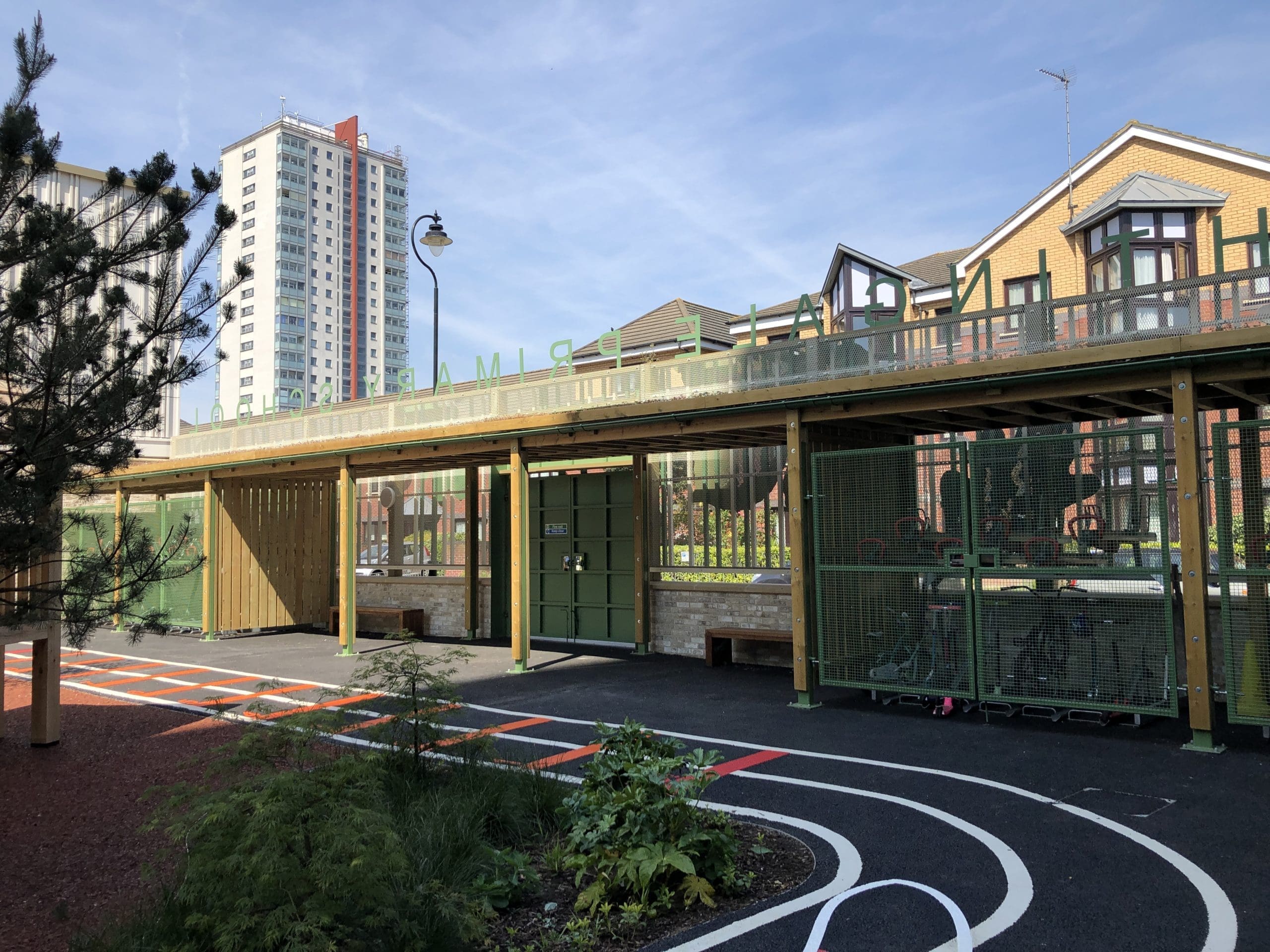 Outdoor wooden canopy with green metal drainage covering two tiered metal bike storage racks and creating cover over school entrance