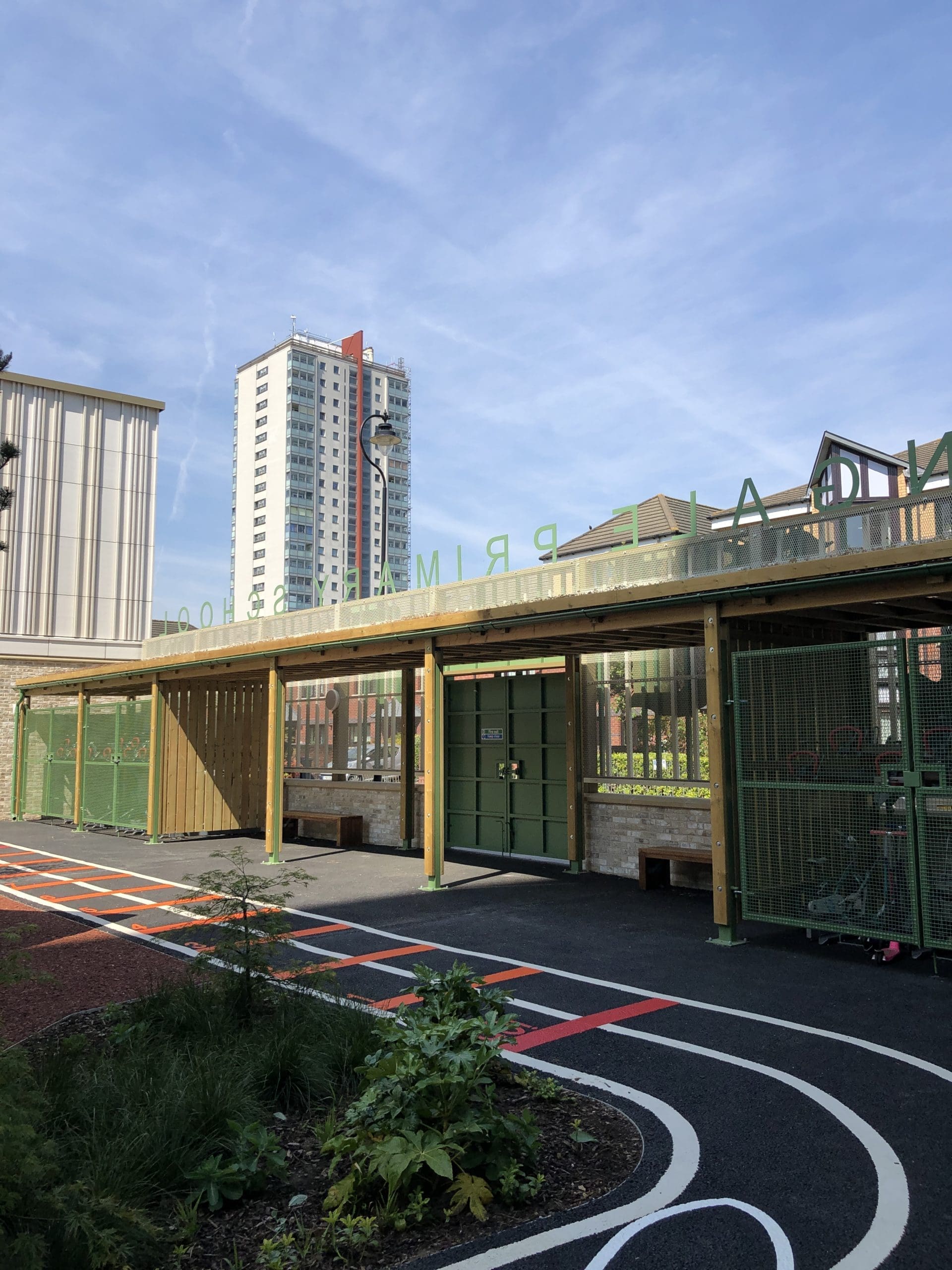 Outdoor wooden canopy with green metal drainage covering two tiered metal bike storage racks and creating cover over school entrance