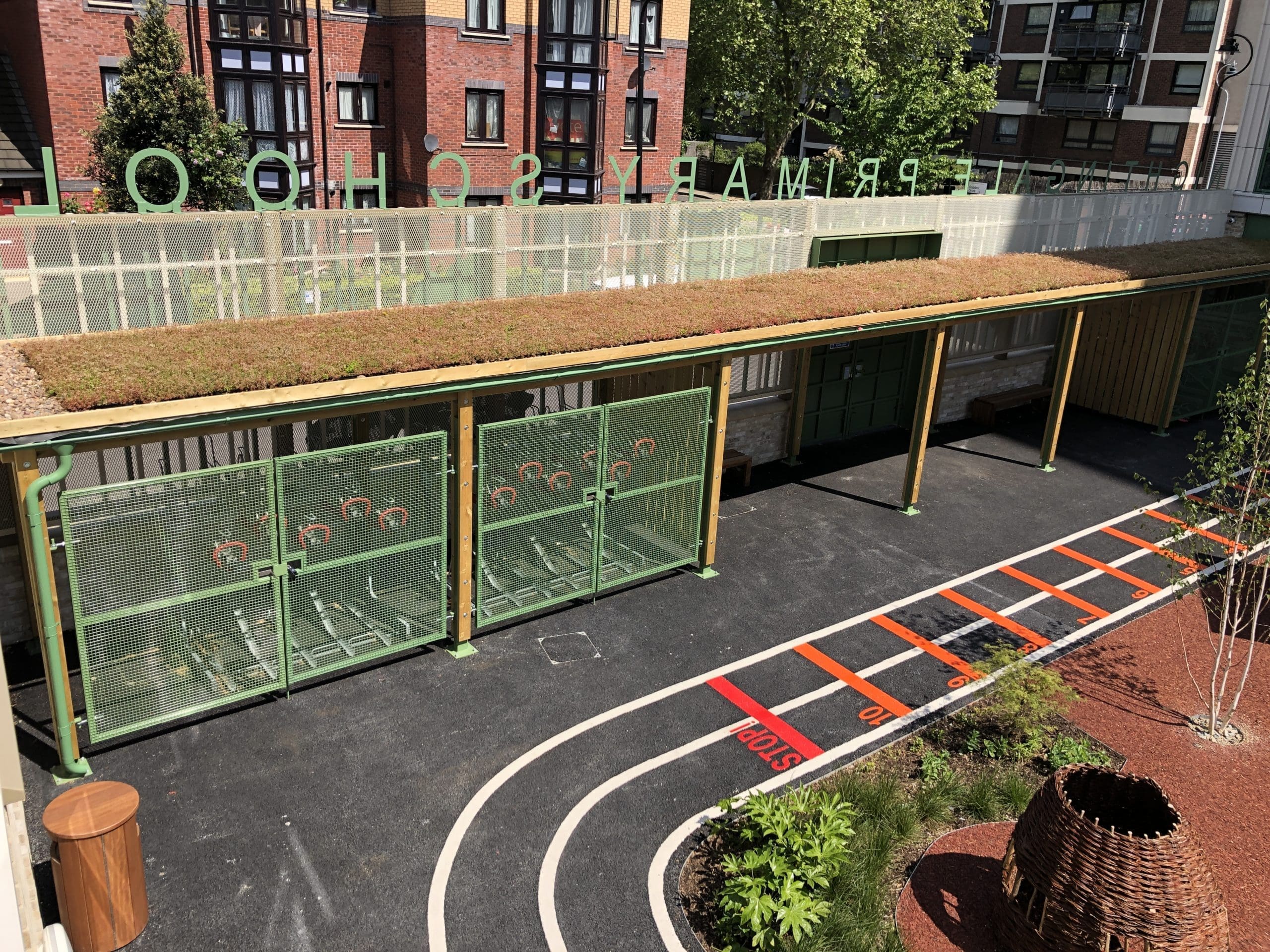 Outdoor wooden canopy with green metal drainage covering two tiered metal bike storage racks and creating cover over school entrance