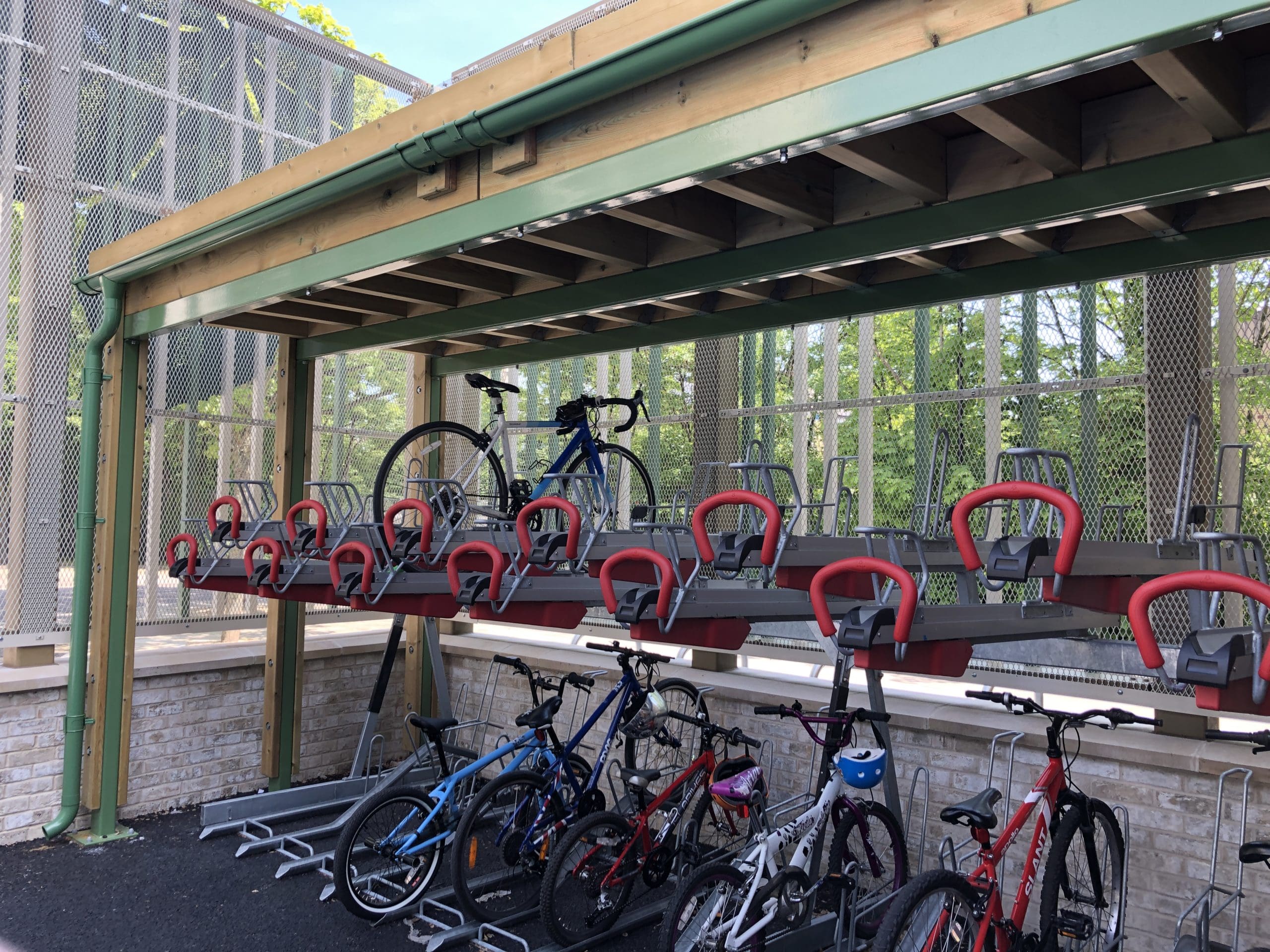 Outdoor wooden canopy with green metal drainage covering two tiered metal bike storage racks