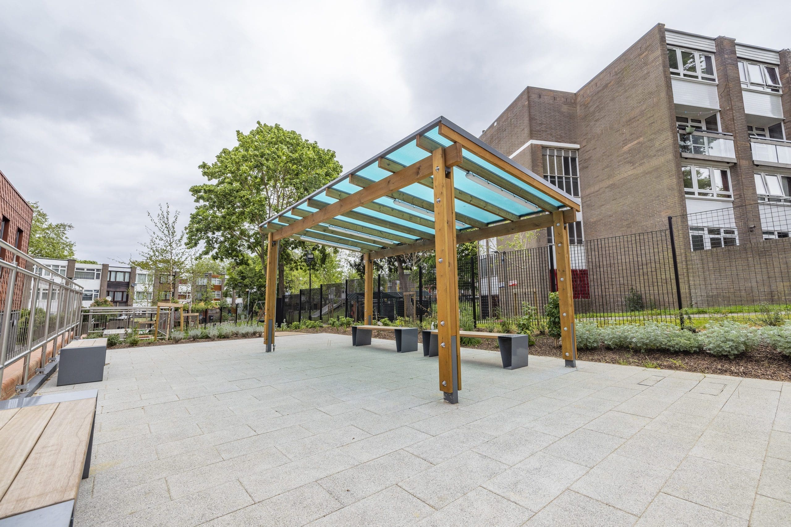 Modern outdoor wooden benches with metal triangular shaped legs under wooden pergola with blue tinted roof