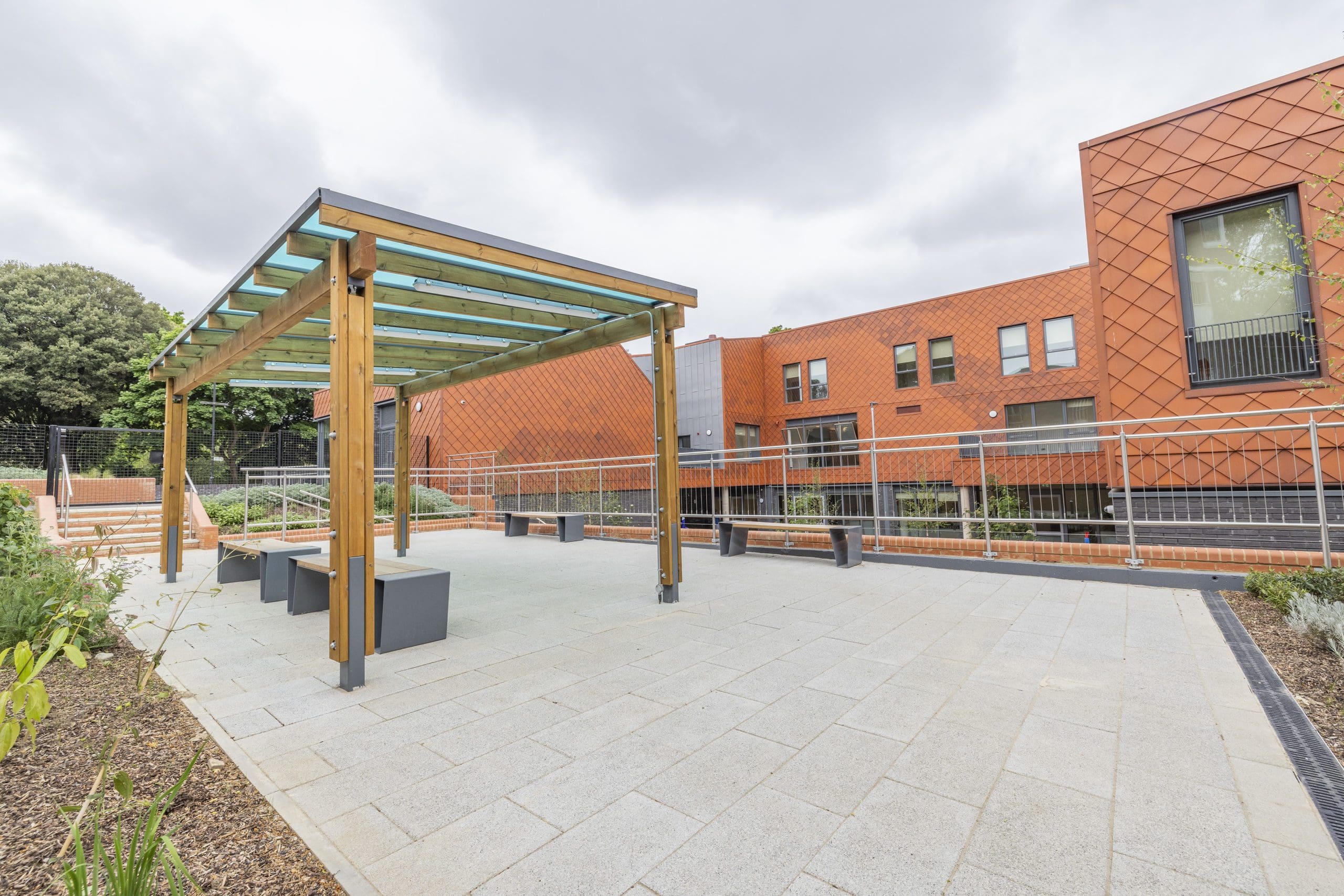 Modern outdoor wooden benches with metal triangular shaped legs under wooden pergola with blue tinted roof