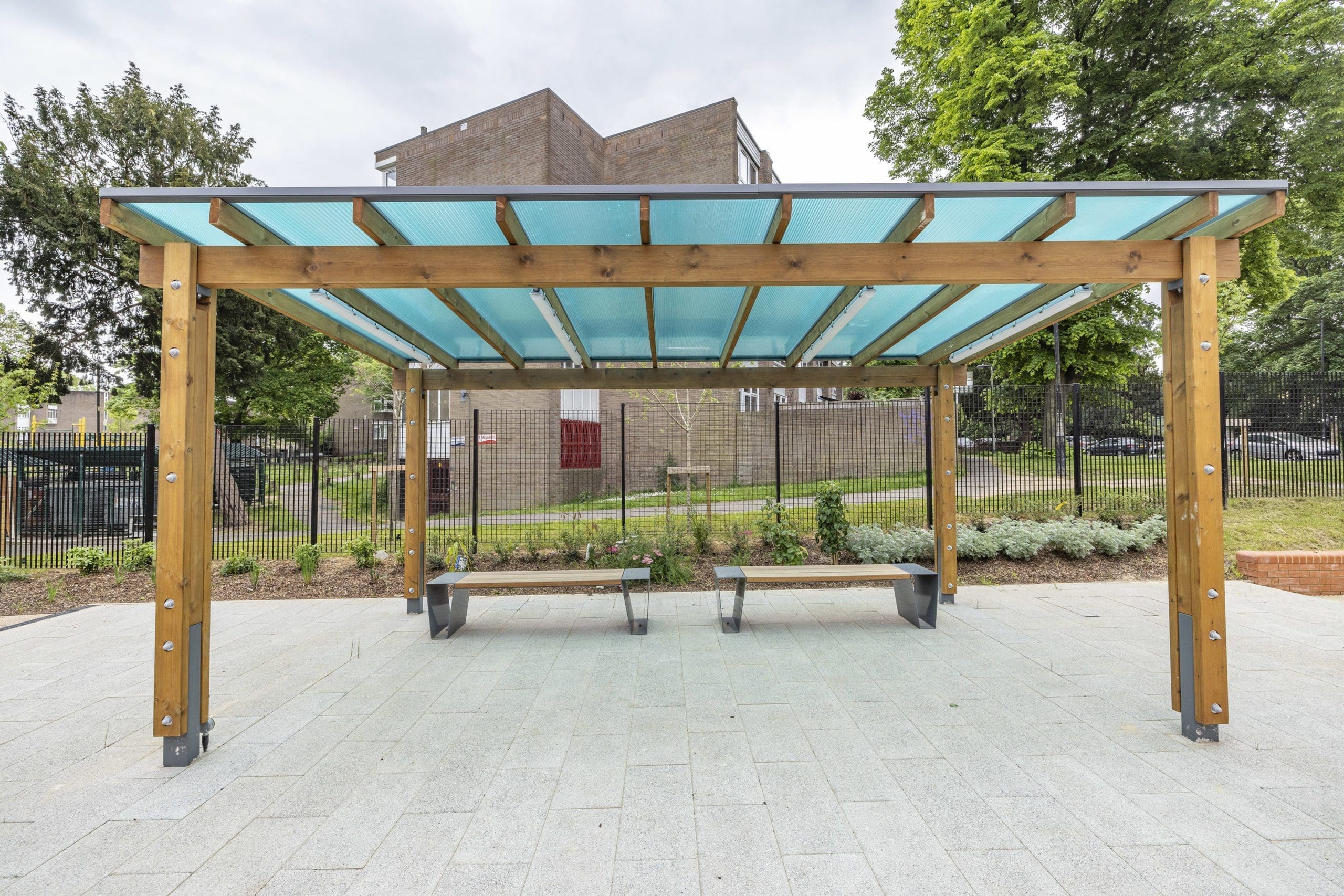 Modern outdoor wooden benches with metal triangular shaped legs under wooden pergola with blue tinted roof